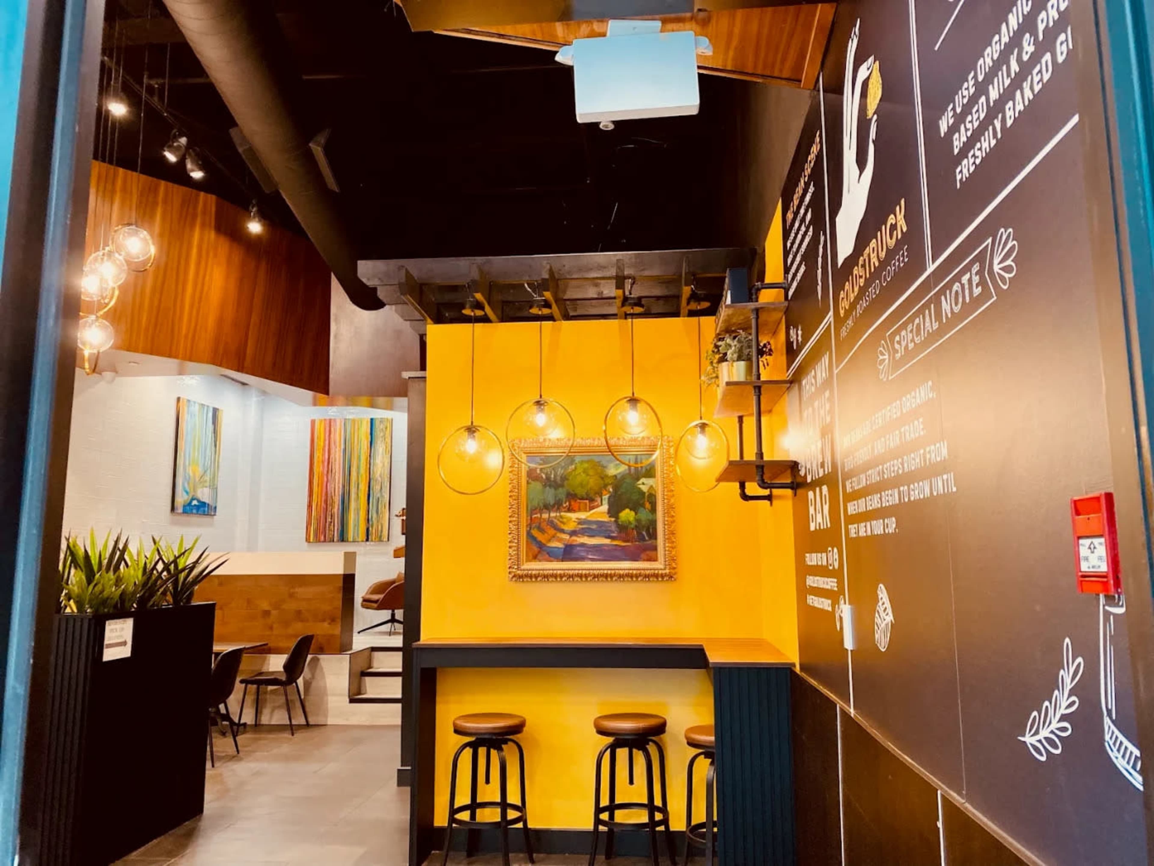 The image shows the interior of a modern café with a bar seating area illuminated by pendant lights and colorful artwork on the walls.