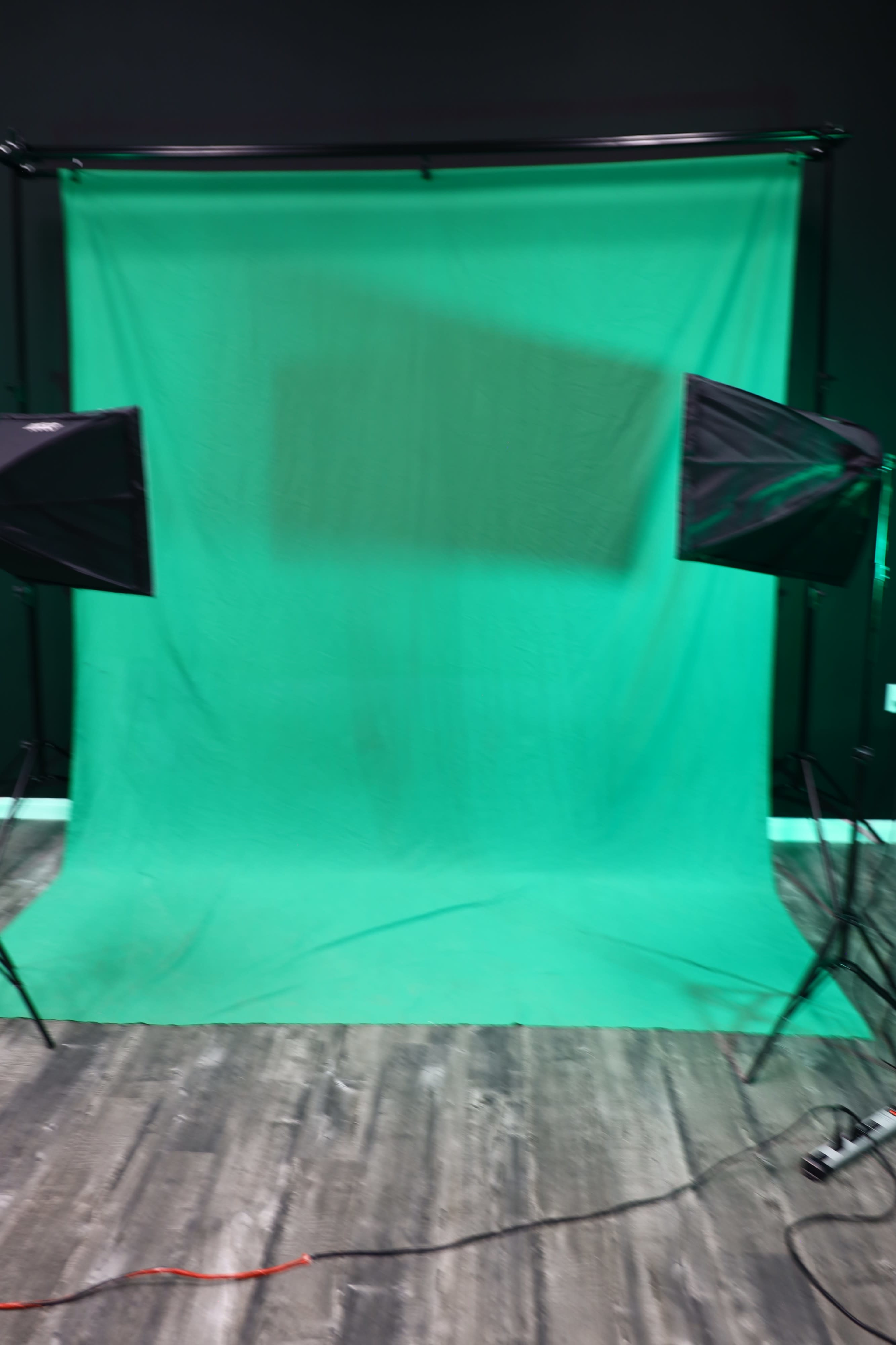 A green screen setup is positioned between two softbox lights in a studio environment.