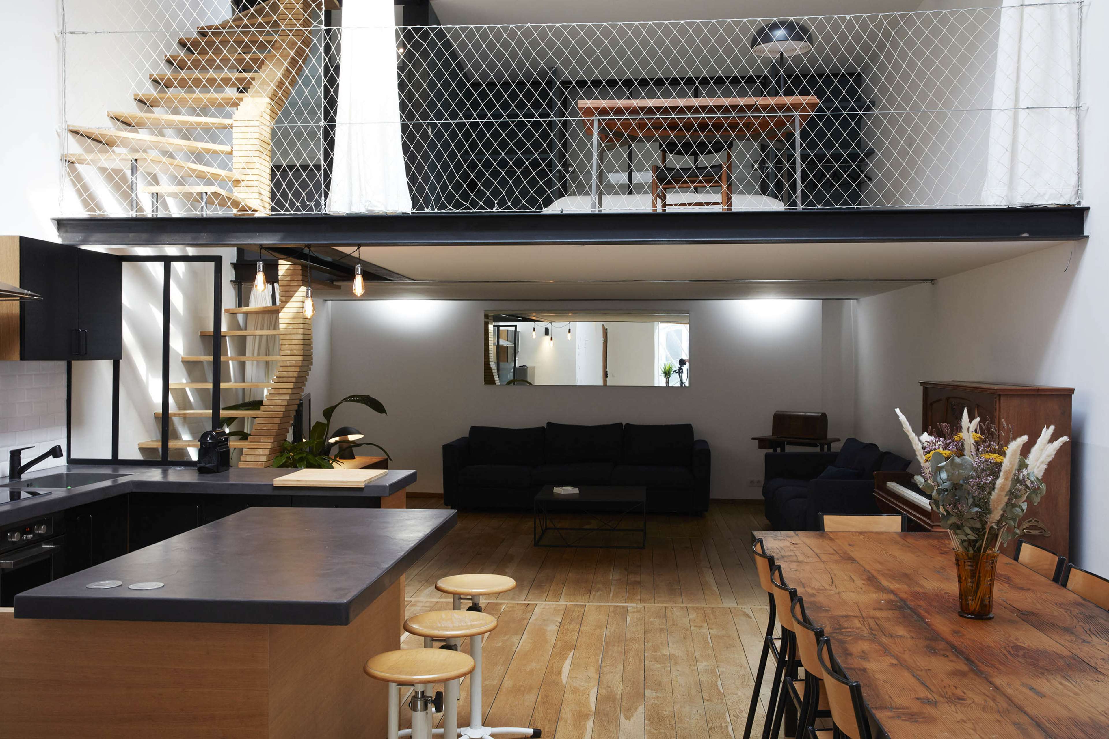 The image features a spacious open-concept living area with a kitchen, dining table, and seating area, along with a staircase leading to a second-floor loft.