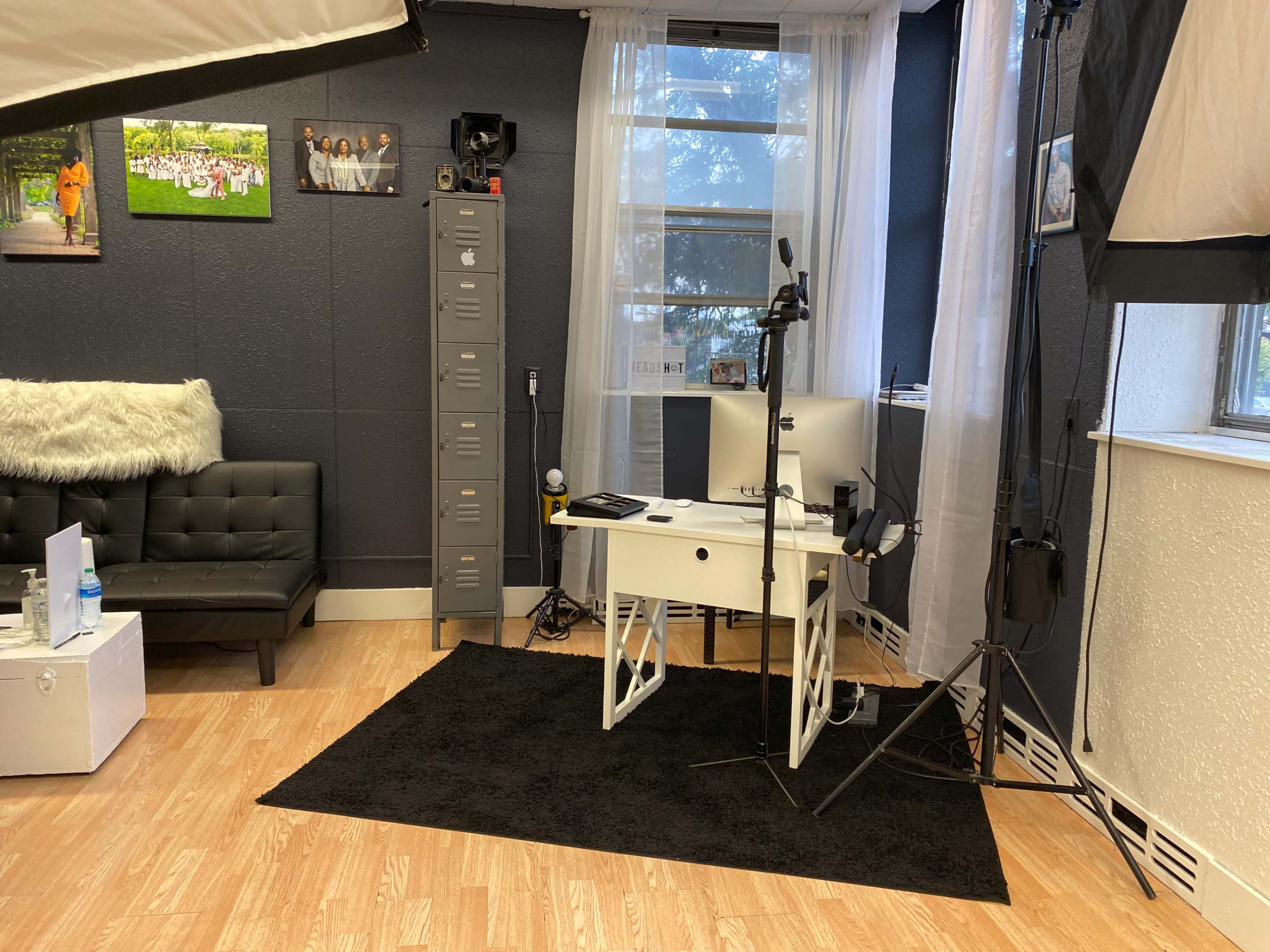 A modern workspace with a black sofa, a desk with a computer, and photography equipment in a well-lit room.