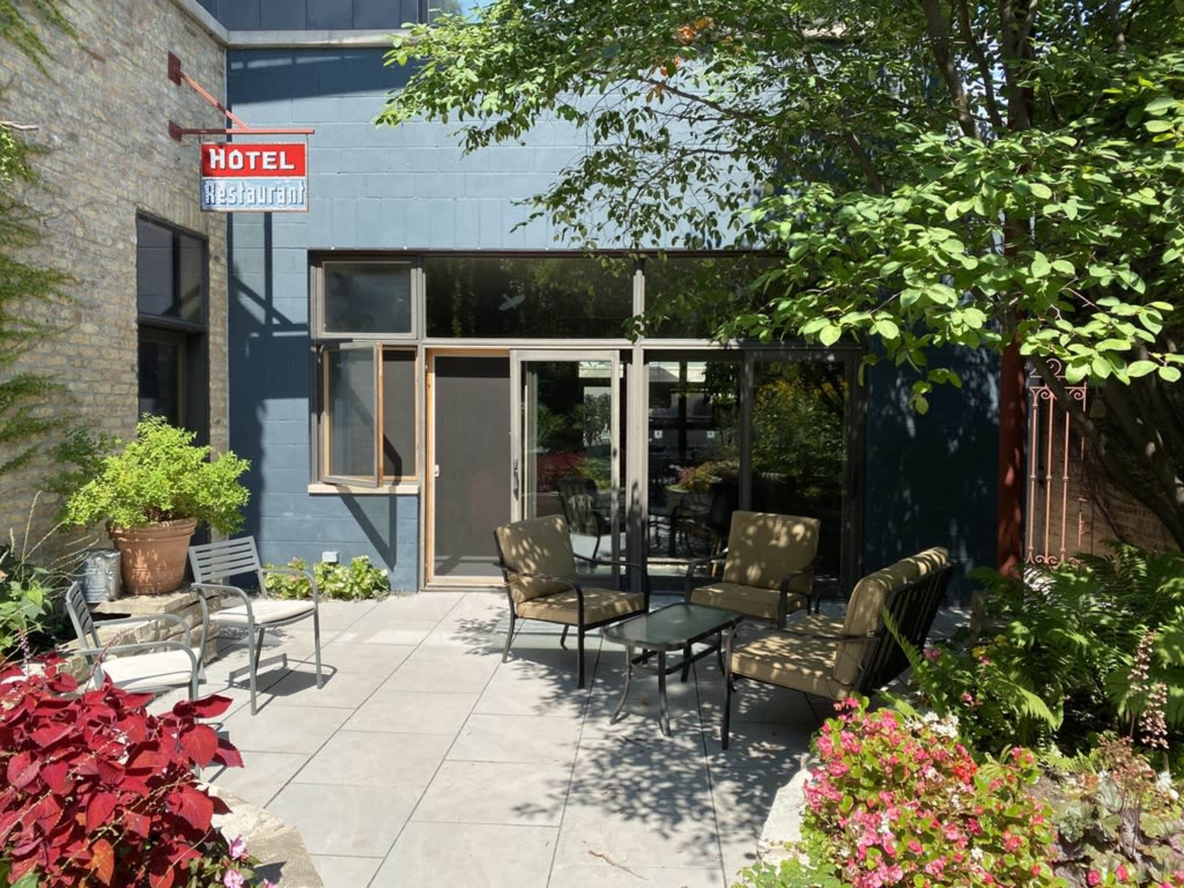 The image shows a patio area of a hotel restaurant featuring outdoor seating surrounded by plants and flowers.