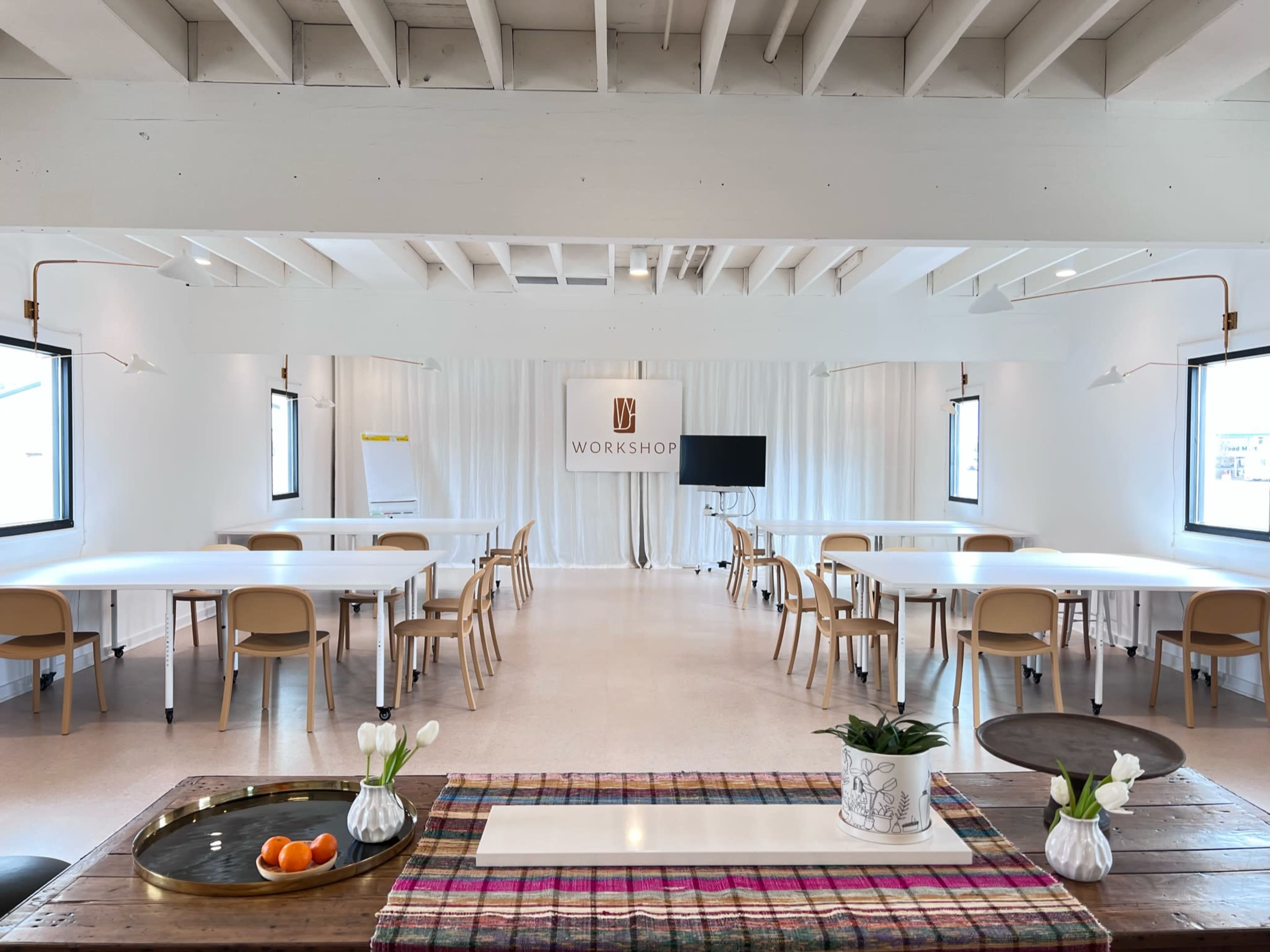 A bright, modern workshop space with several tables, chairs, and a screen at the front, all arranged in a clean, organized manner.