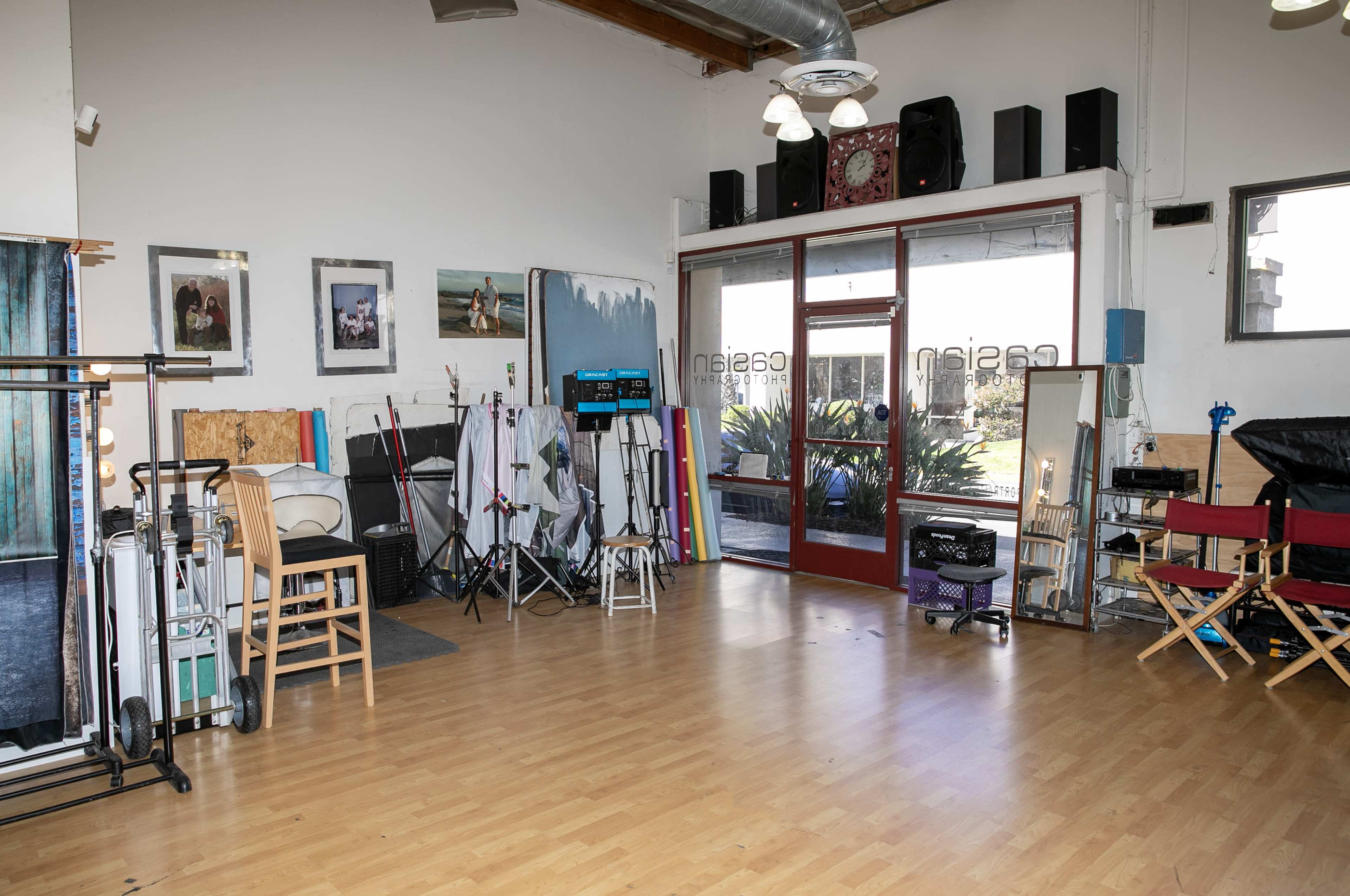 A spacious studio with various photography equipment, chairs, and large windows allowing natural light to enter.