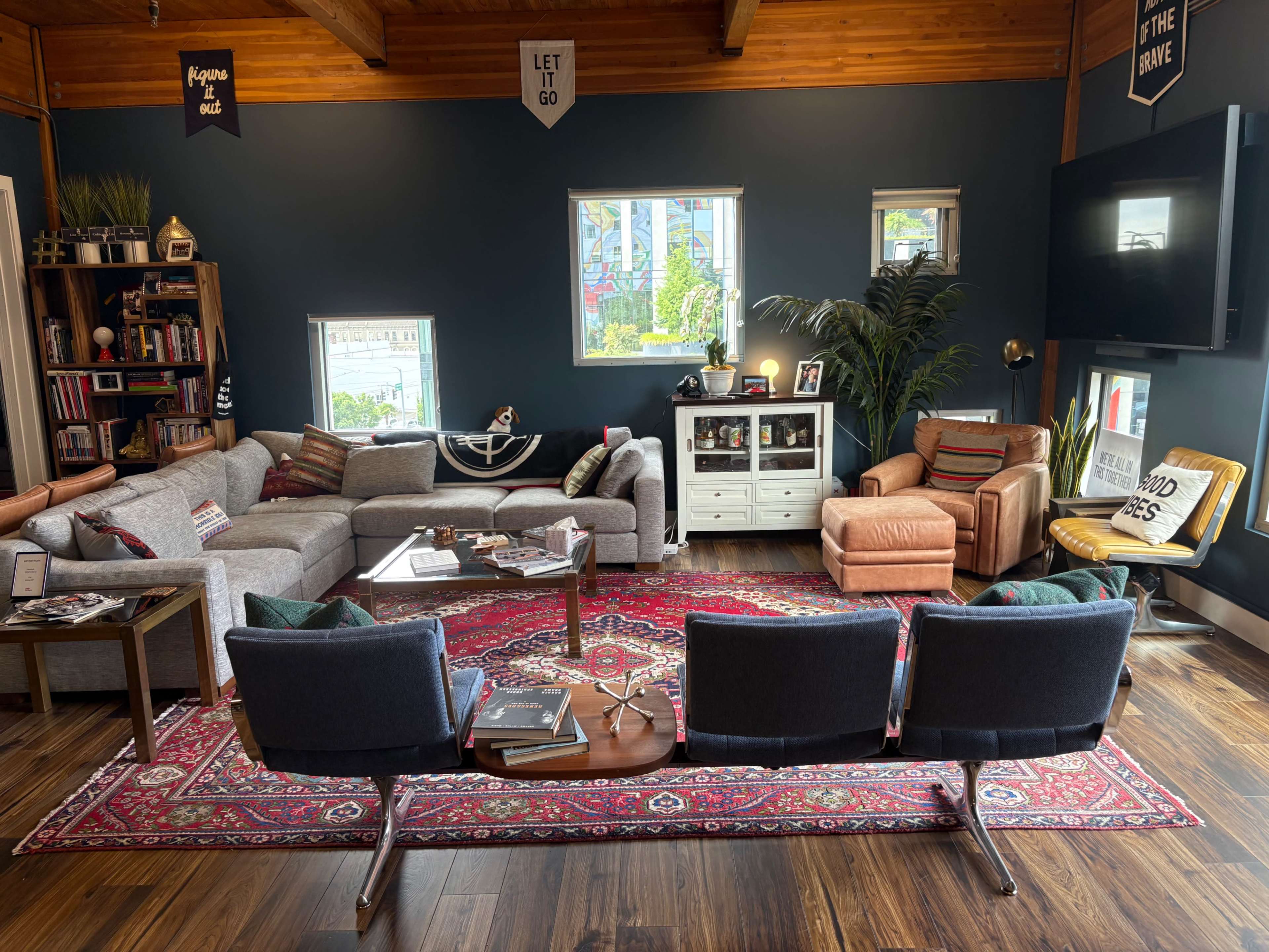 A modern living room features a gray sectional sofa, a wooden coffee table, and various decorative elements against a dark blue wall.