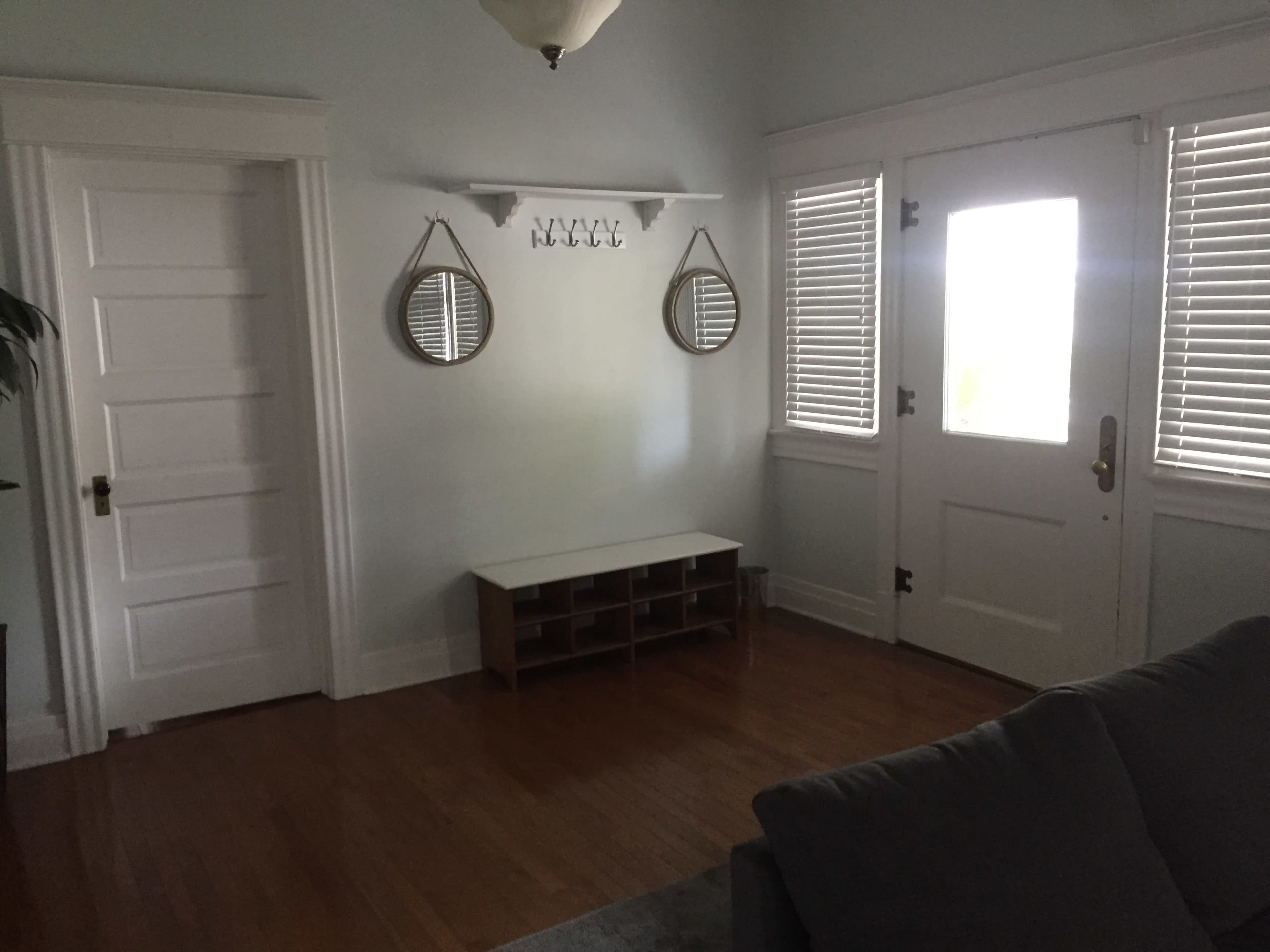 The room features a wooden floor with a bench, two mirrors above it, and a door with window panes beside it.