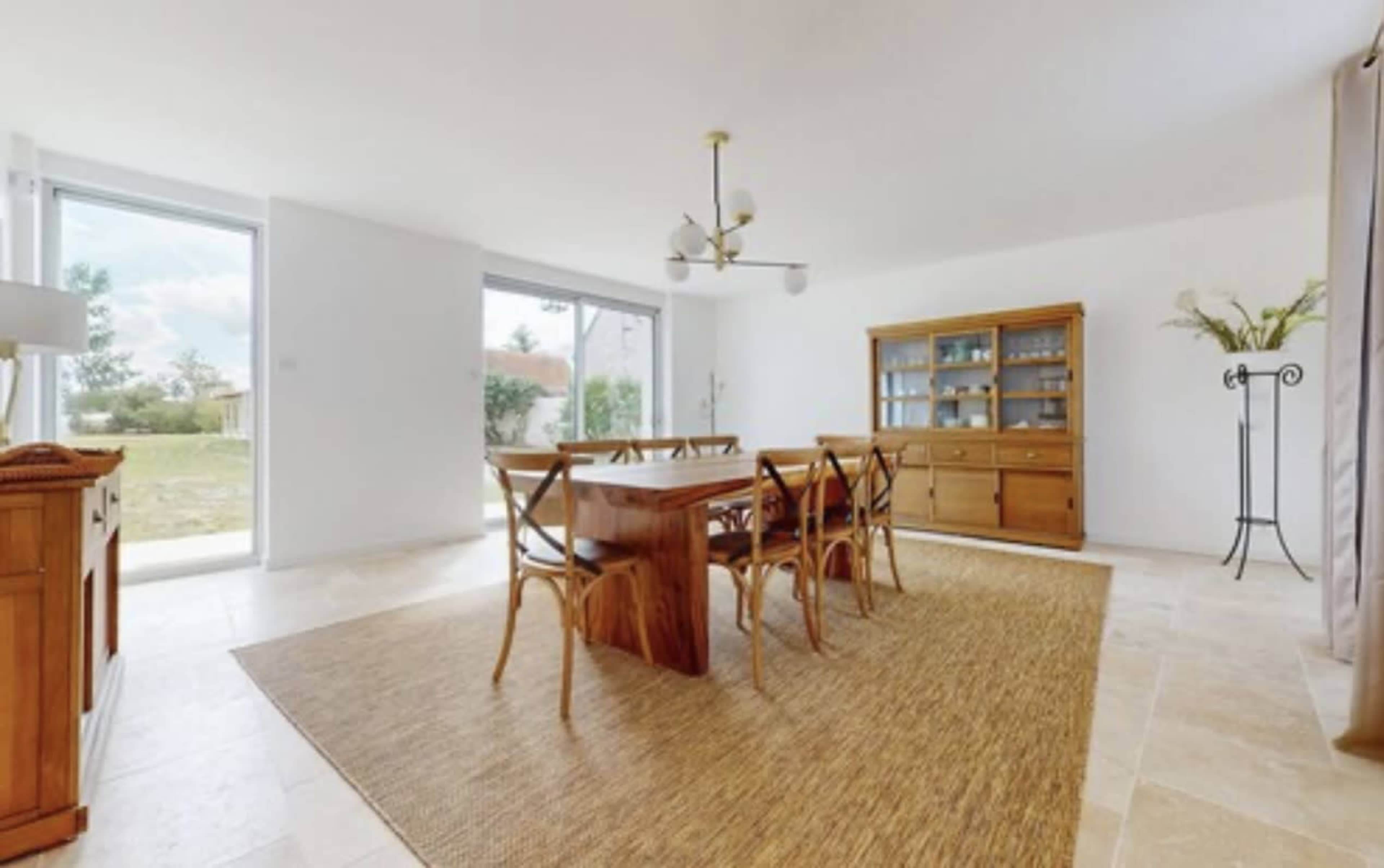 The image shows a spacious dining area featuring a wooden table with six chairs, a sideboard, and large windows that provide natural light.