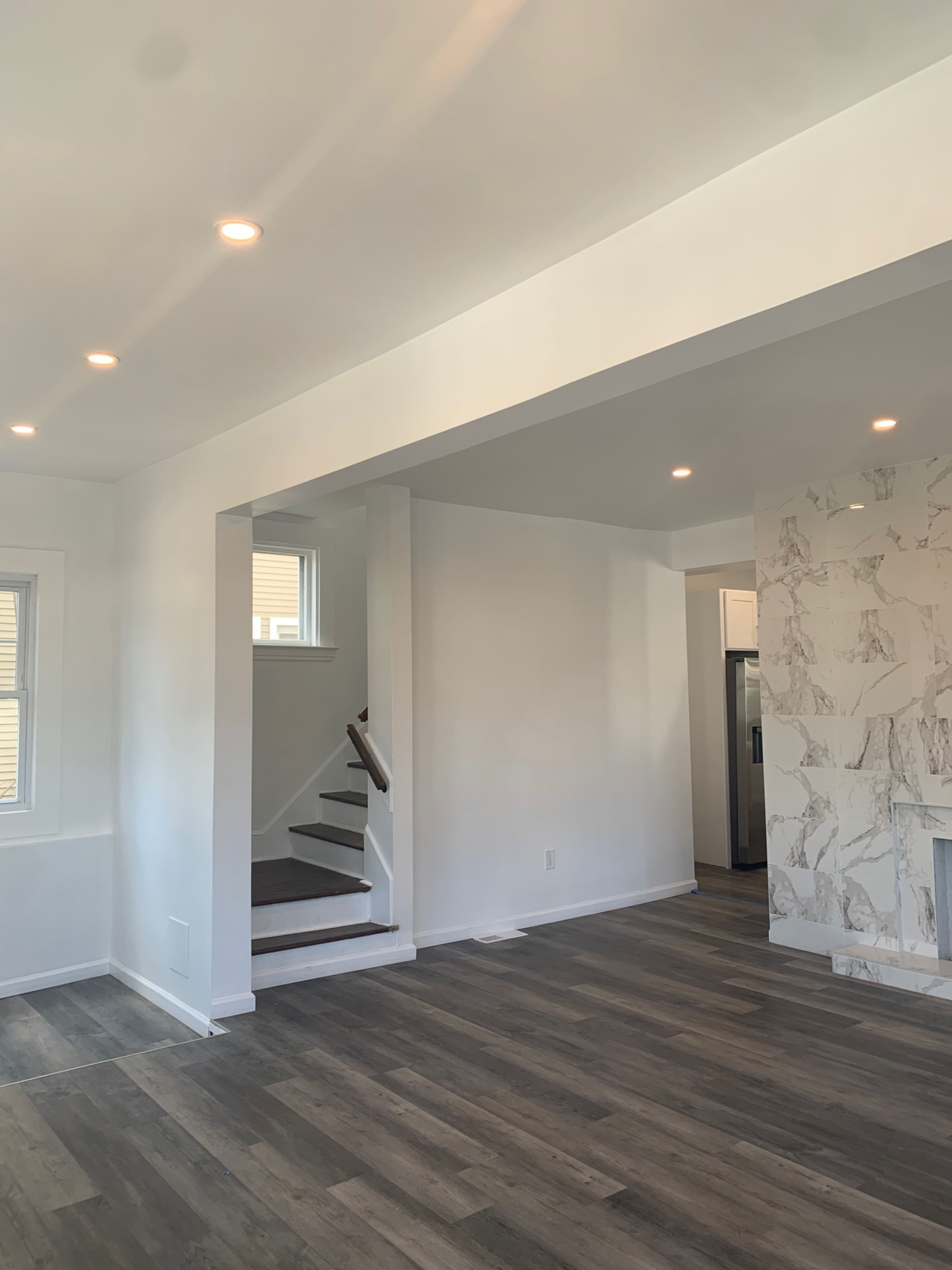 A bright, open living space features white walls, wooden flooring, and a staircase leading to another level.