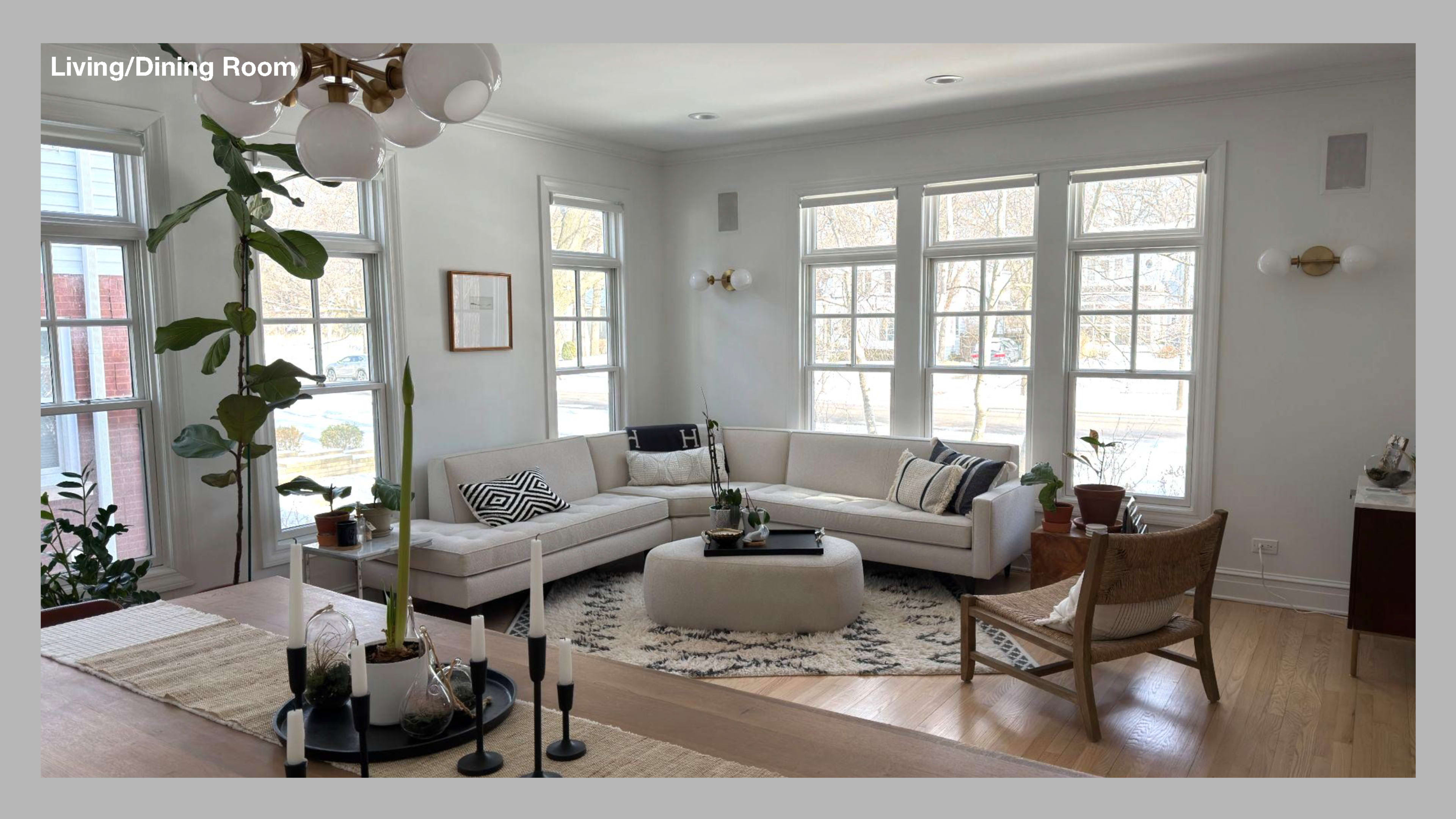 A bright living and dining room features a large sectional sofa, a round coffee table, and several windows allowing natural light to fill the space.