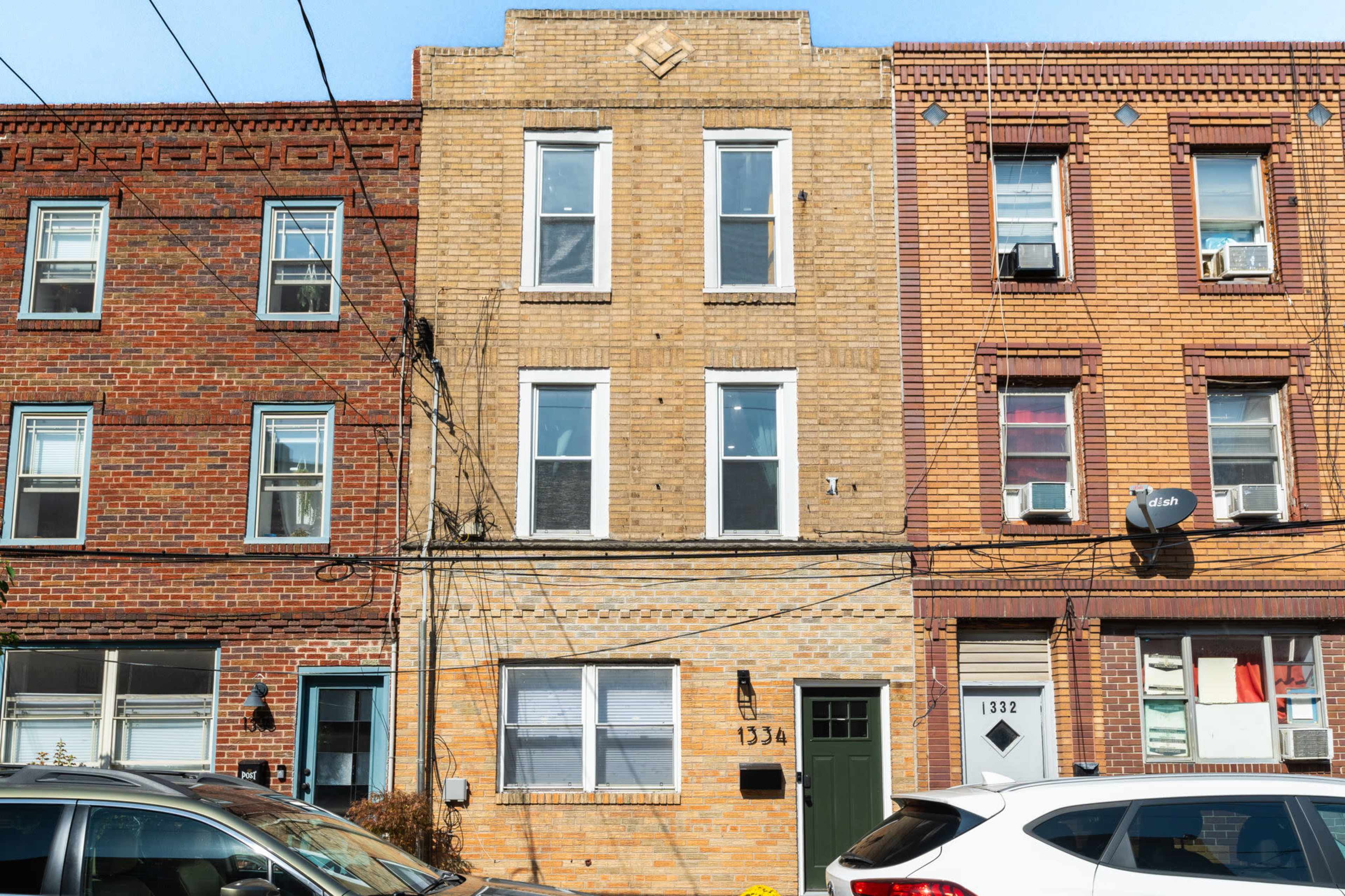 The image shows a row of three multi-story brick residential buildings with street-facing windows and a parked car in front.