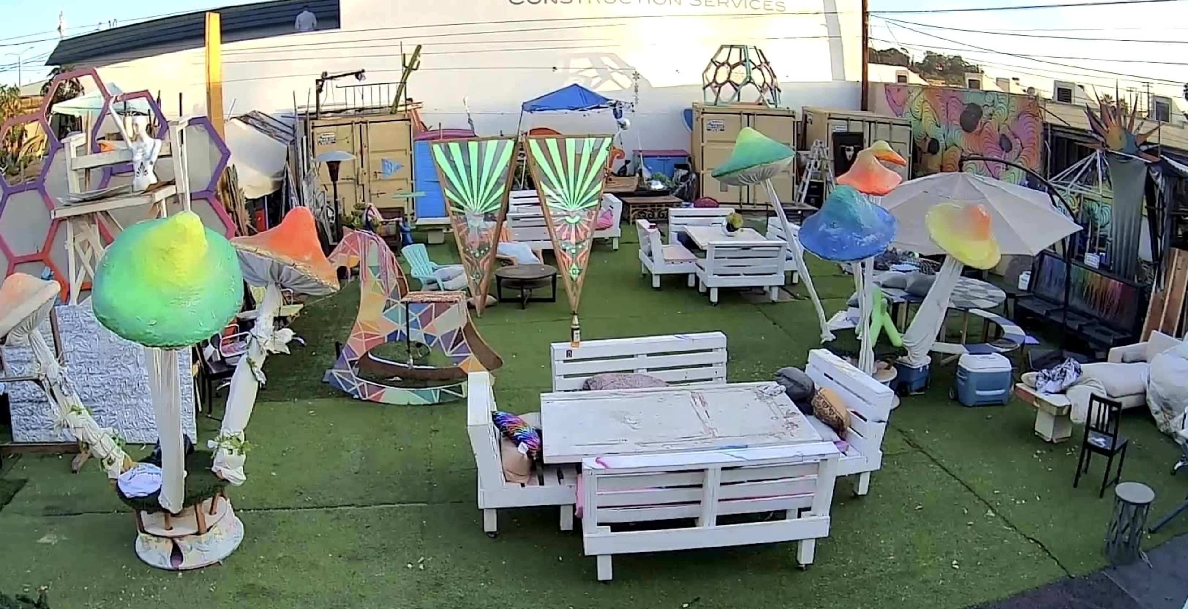 A colorful outdoor space with artistic sculptures, seating arrangements on artificial grass, and various decorative elements.