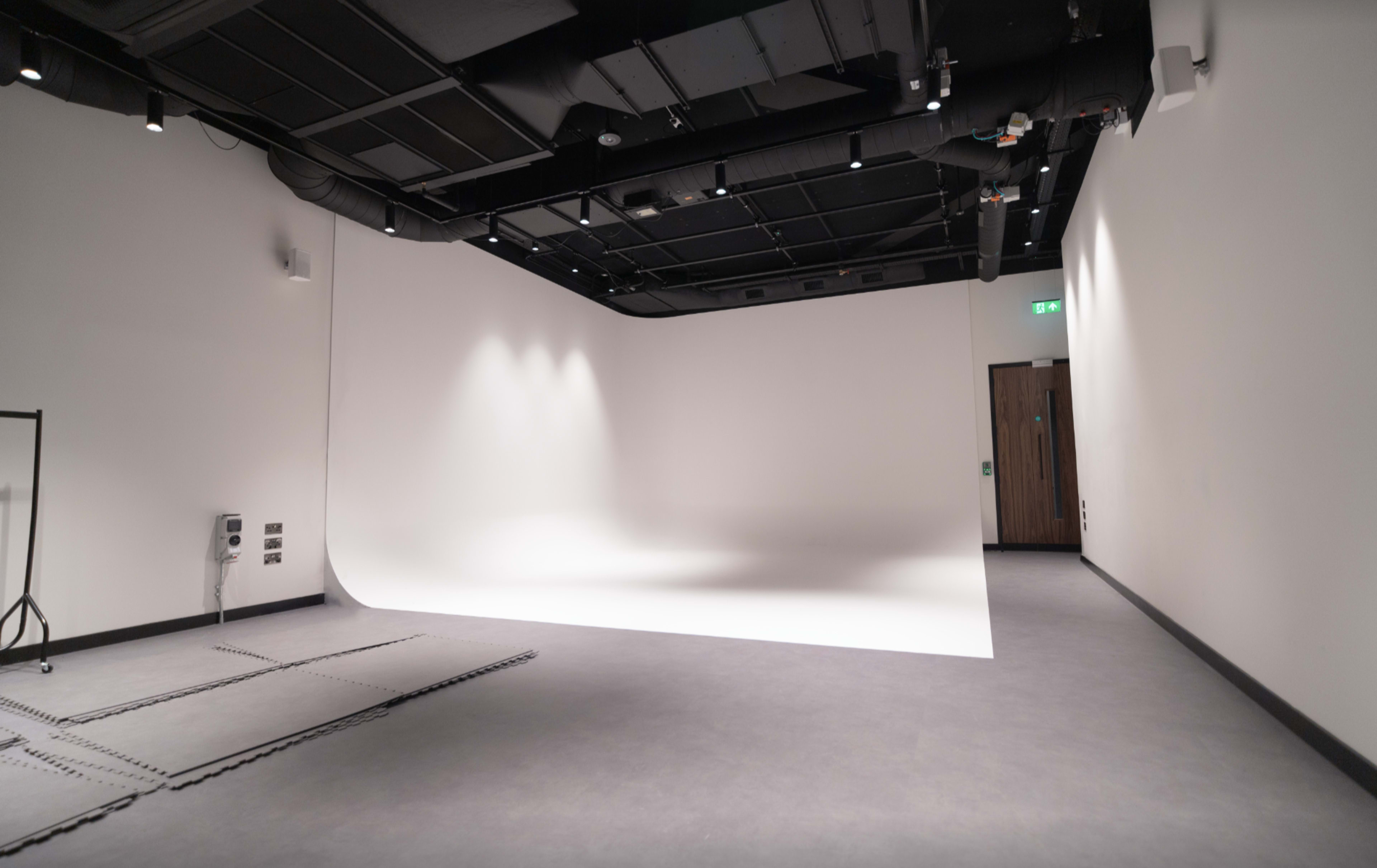 The image shows a spacious, empty studio with a seamless white backdrop and minimal furniture.