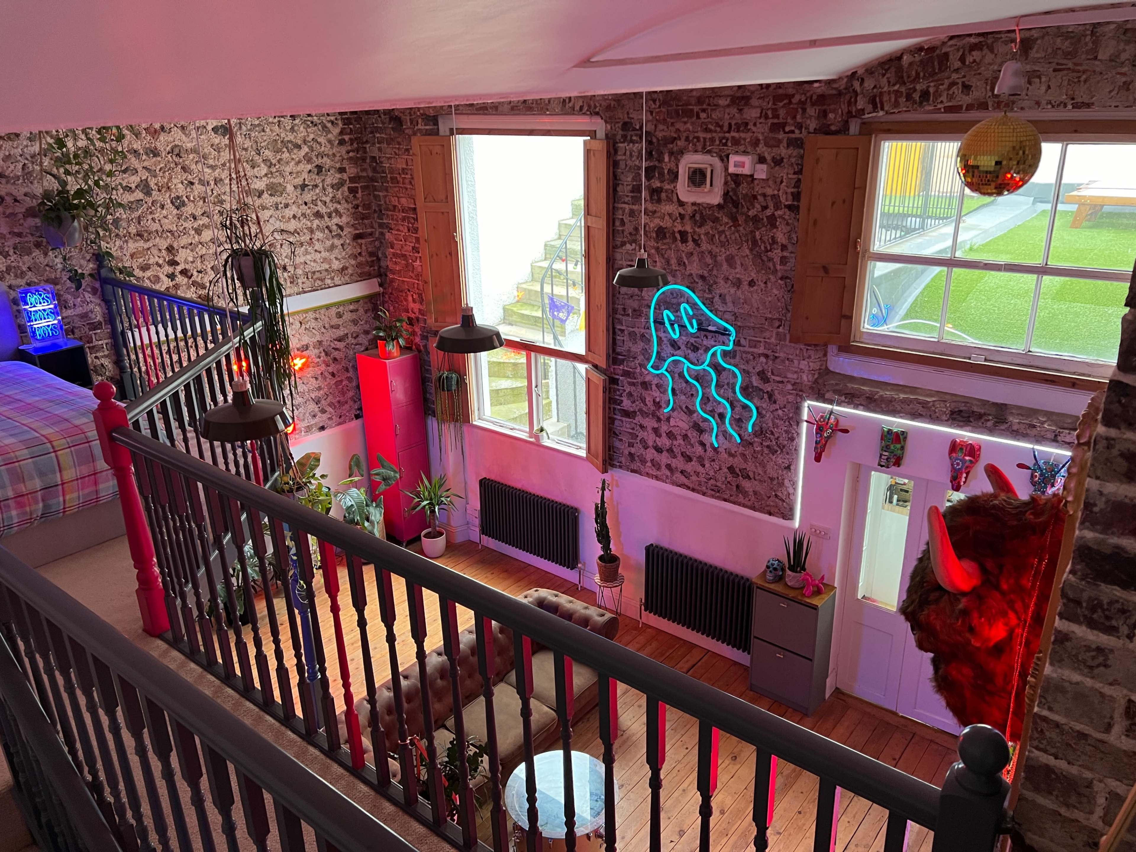 A vibrant, creatively decorated room with stone walls, featuring plants, colorful lighting, and a neon jellyfish design on the wall.