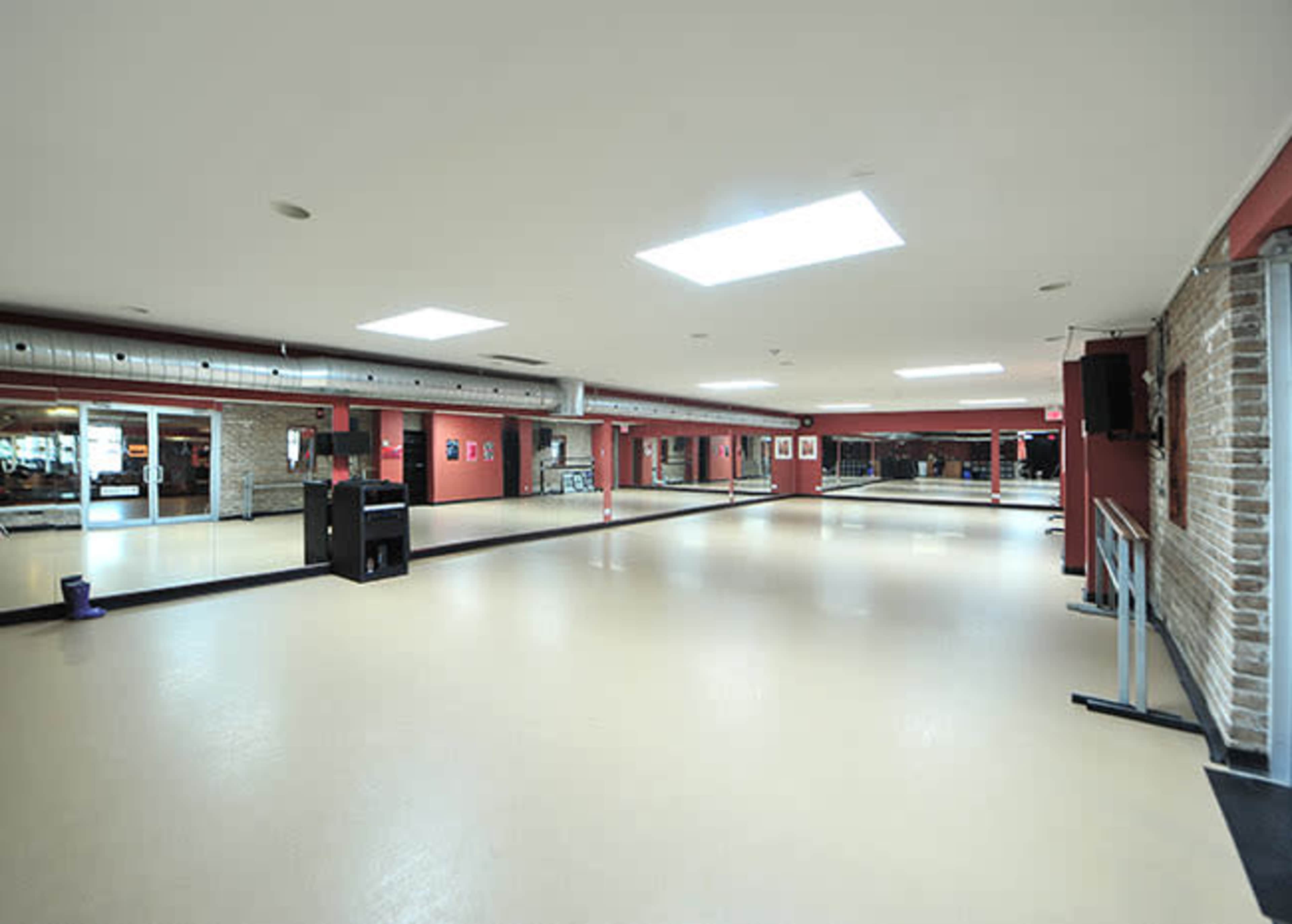 The image shows a spacious dance studio with large mirrors, a light-colored floor, and a skylight illuminating the area.