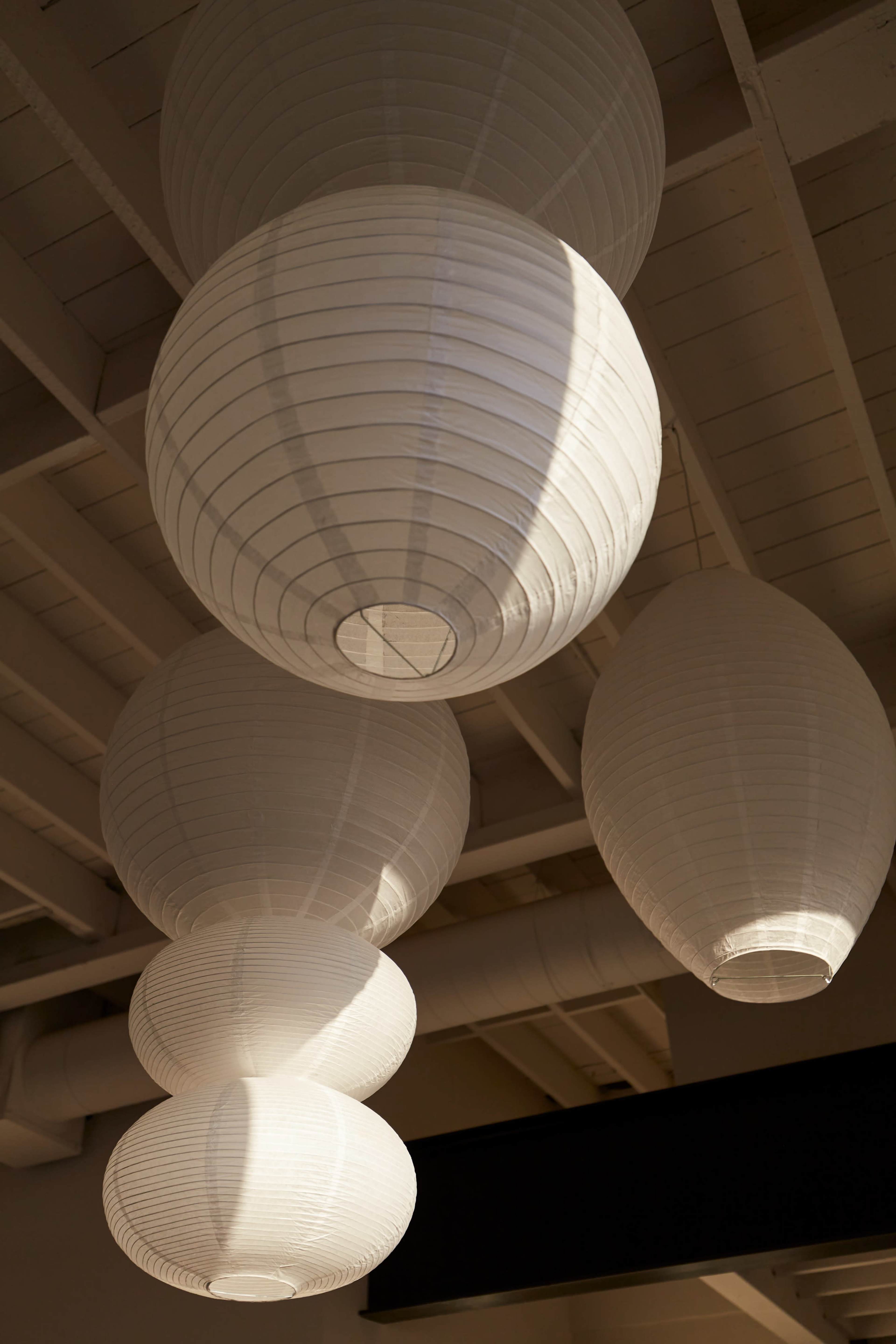 The image shows several white paper lanterns hanging from a ceiling with exposed beams.