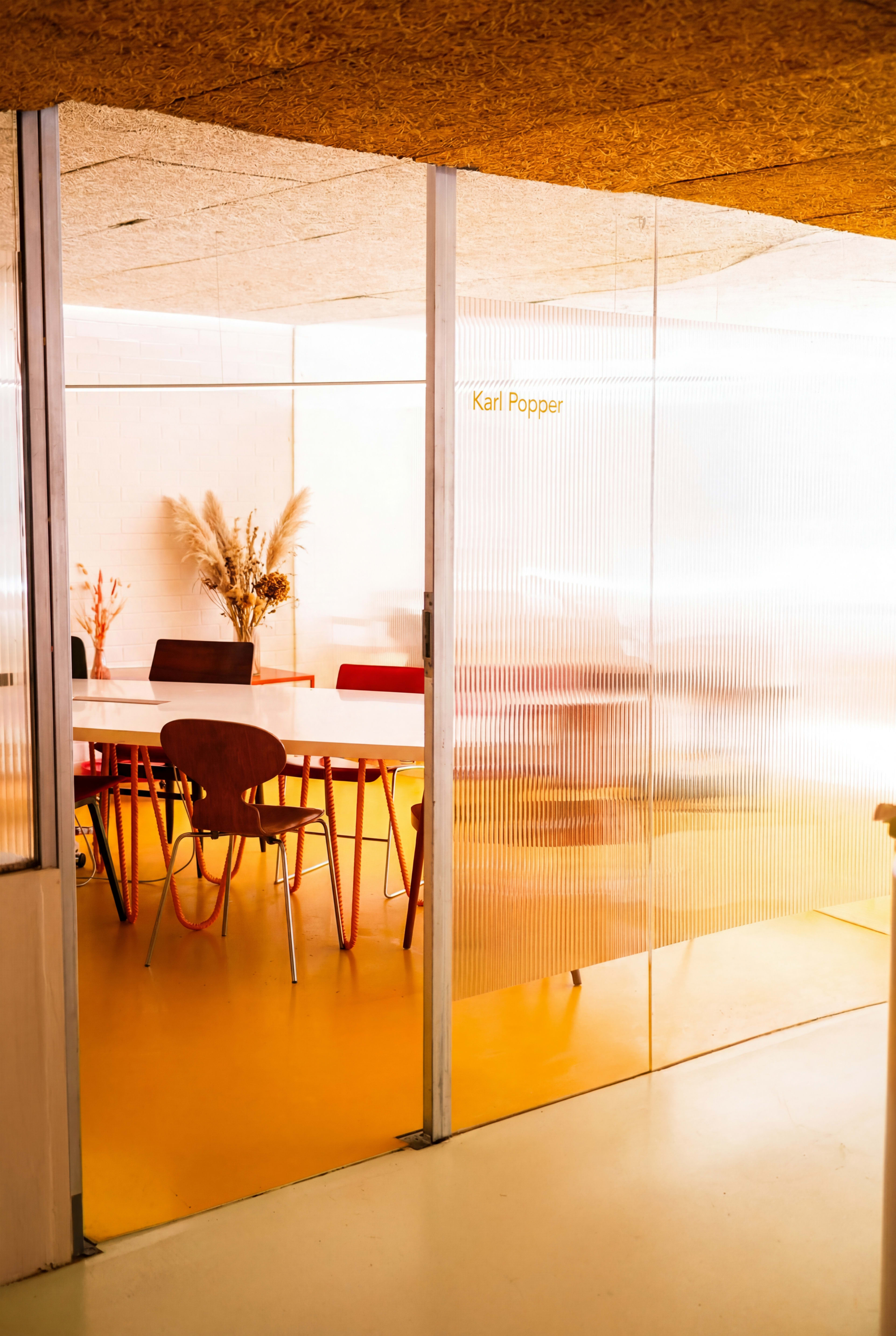 A brightly lit meeting room features a table surrounded by colorful chairs and decorative plant arrangements.