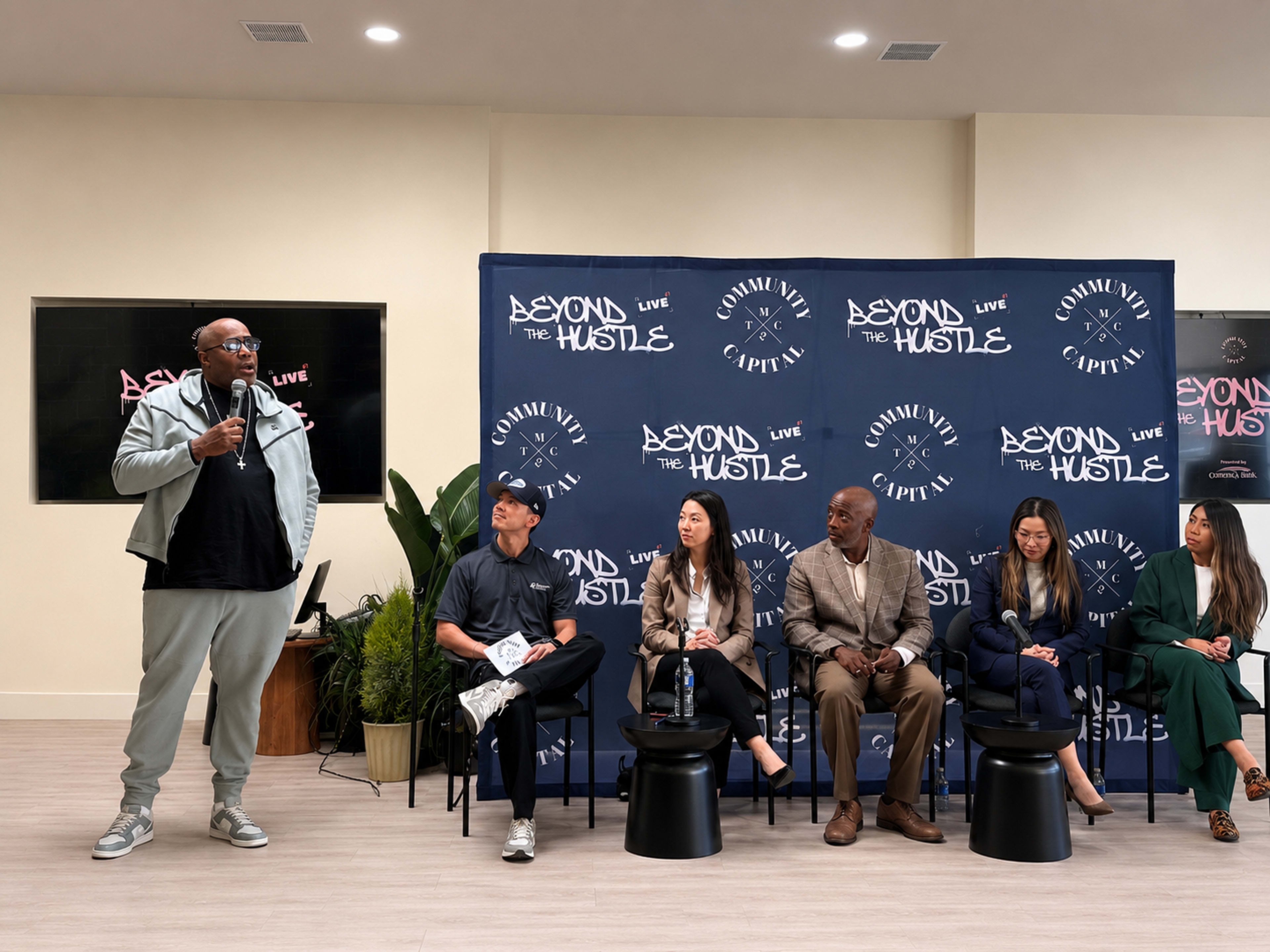 A speaker stands in front of a panel while addressing an audience at an event titled "Beyond the Hustle."