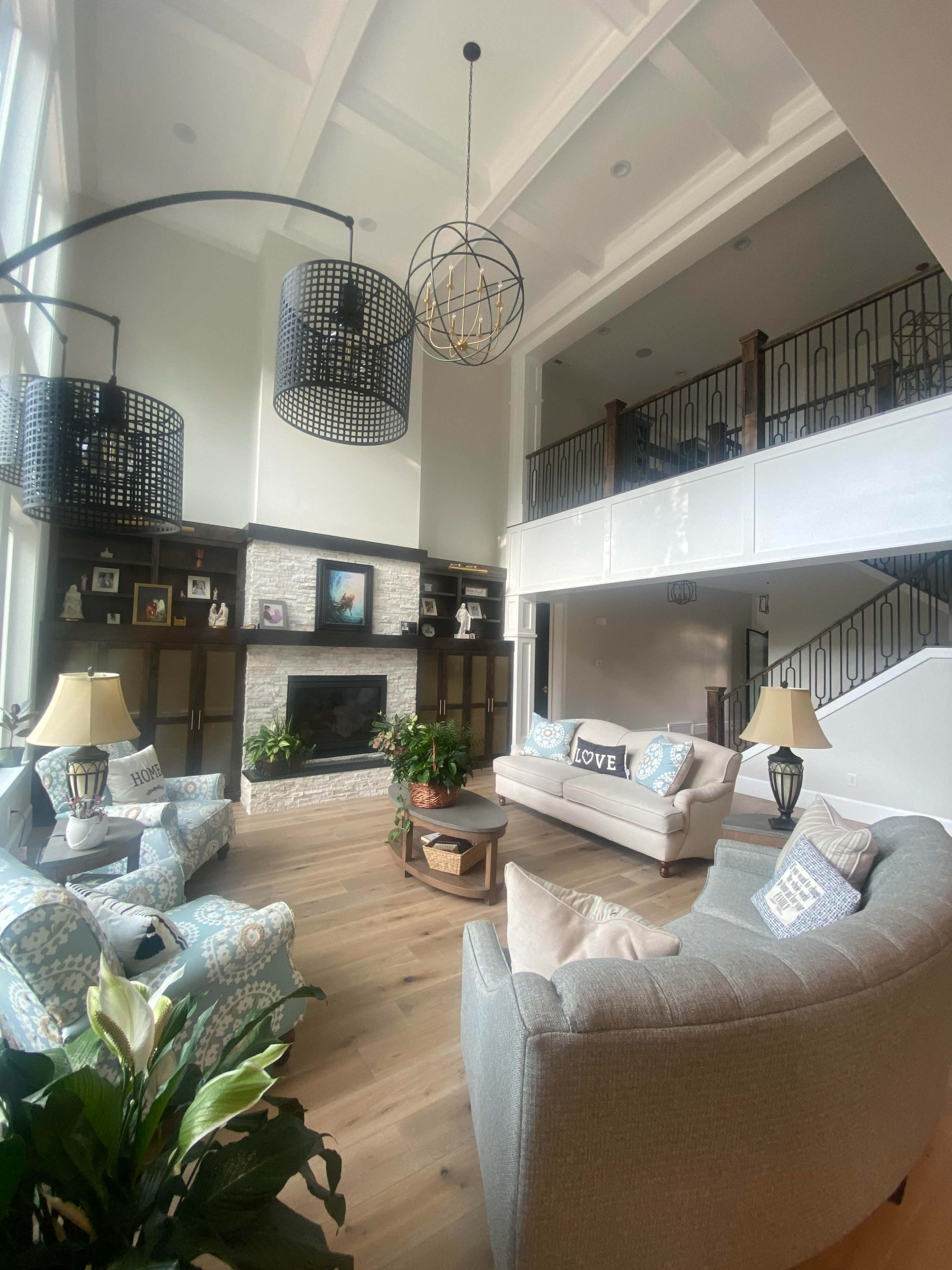 The living room features a high ceiling with large windows, a stone fireplace, and comfortable seating arranged around a coffee table.