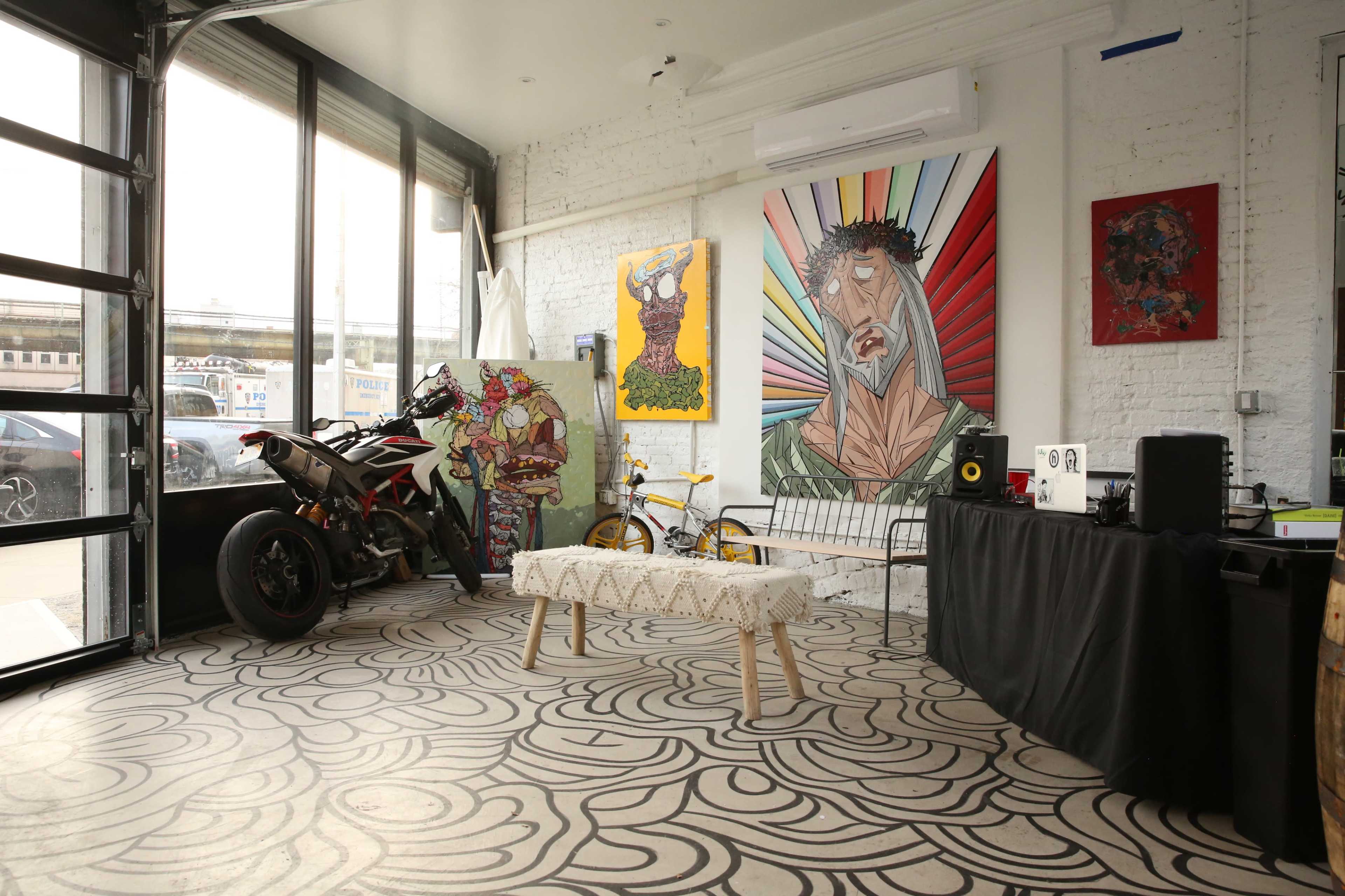 An interior space featuring a motorcycle, colorful artwork on the walls, a wooden bench, and a black table with equipment.