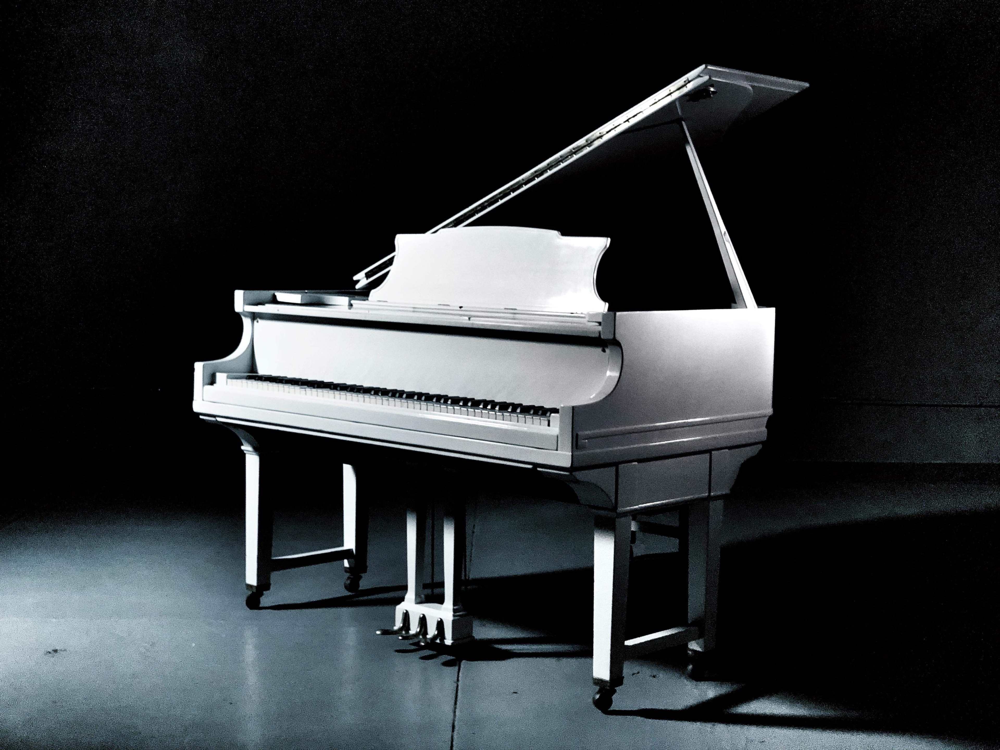 A white grand piano is positioned in a dimly lit room.