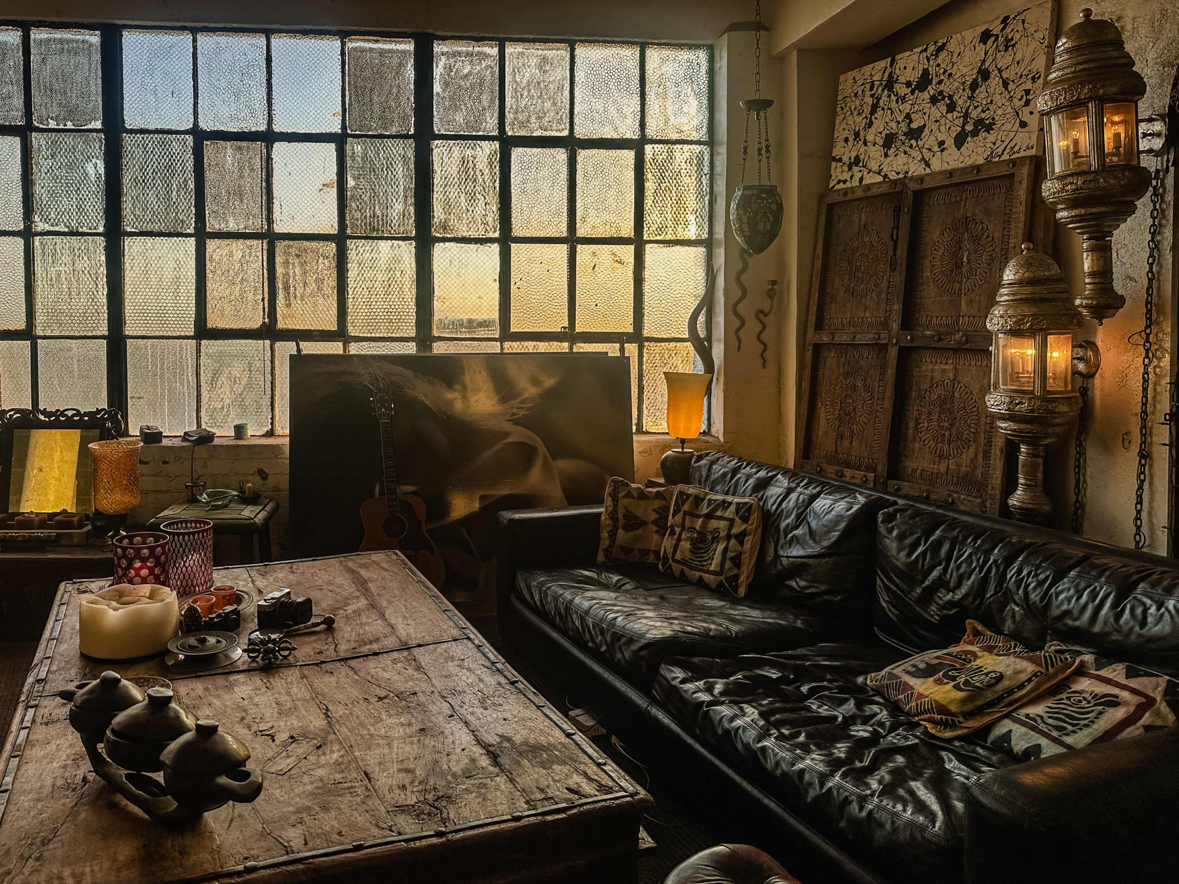 The scene features a cozy, vintage living room with a leather couch, a rustic wooden table, decorative lanterns, and large windows that allow soft light to filter through.