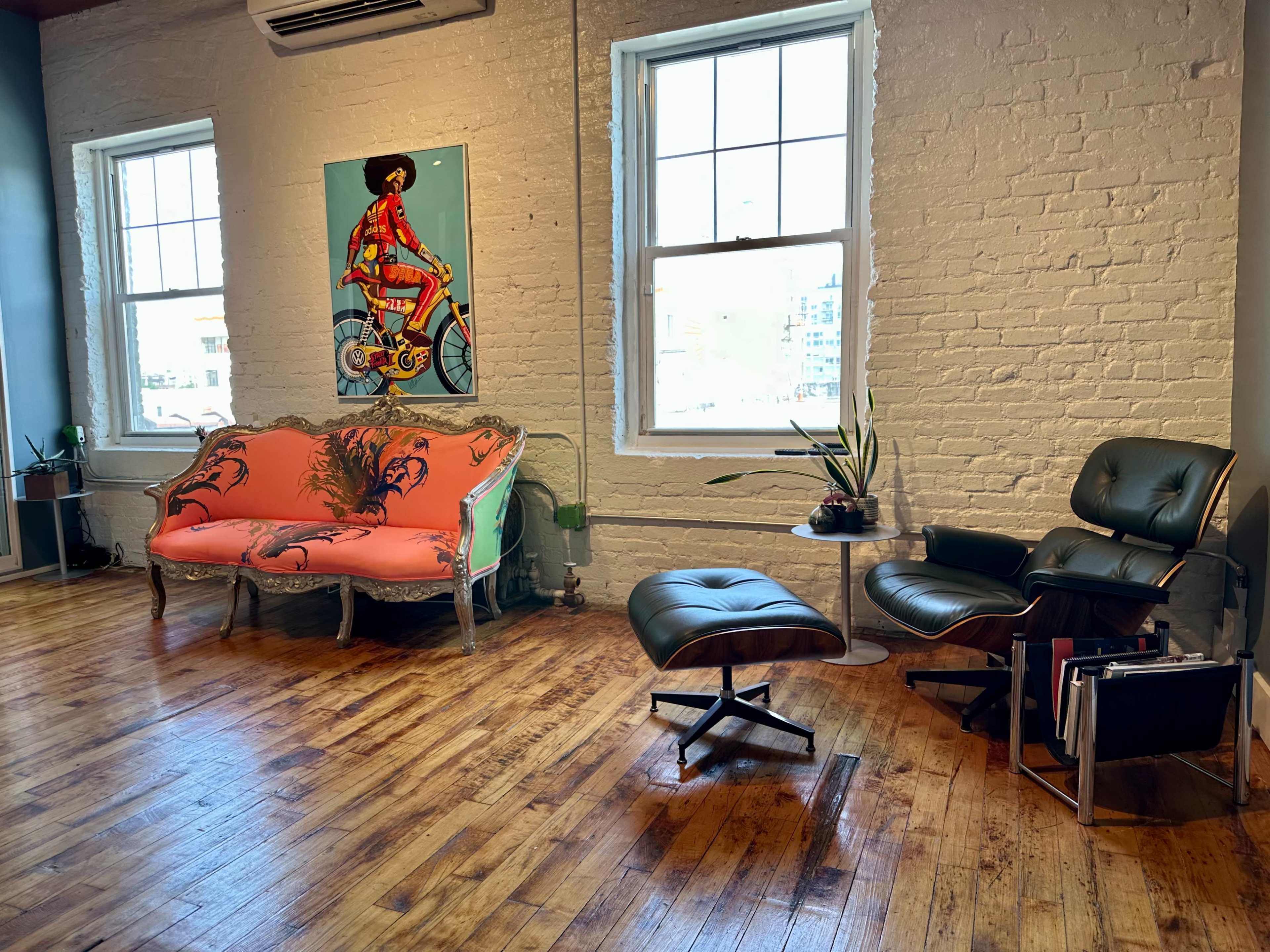 A bright room with a pink and orange sofa featuring a tiger design, an Eames-style lounge chair and ottoman, and large windows allowing natural light to enter.