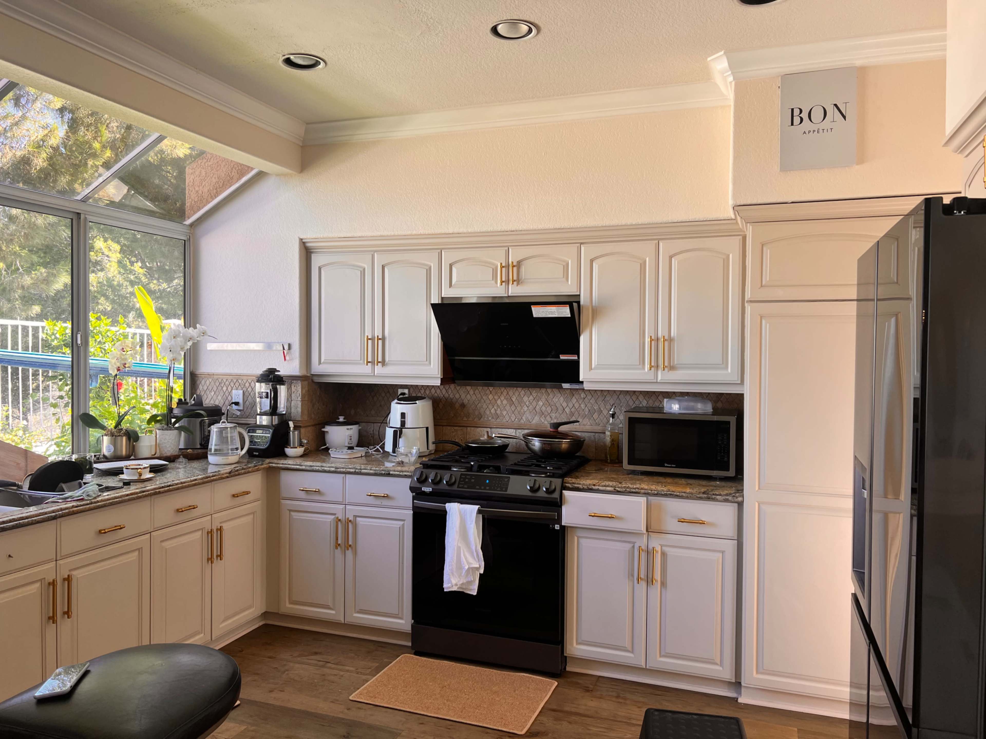 A modern kitchen with white cabinetry, a black stove, a microwave, and various kitchen appliances arranged along the countertop.
