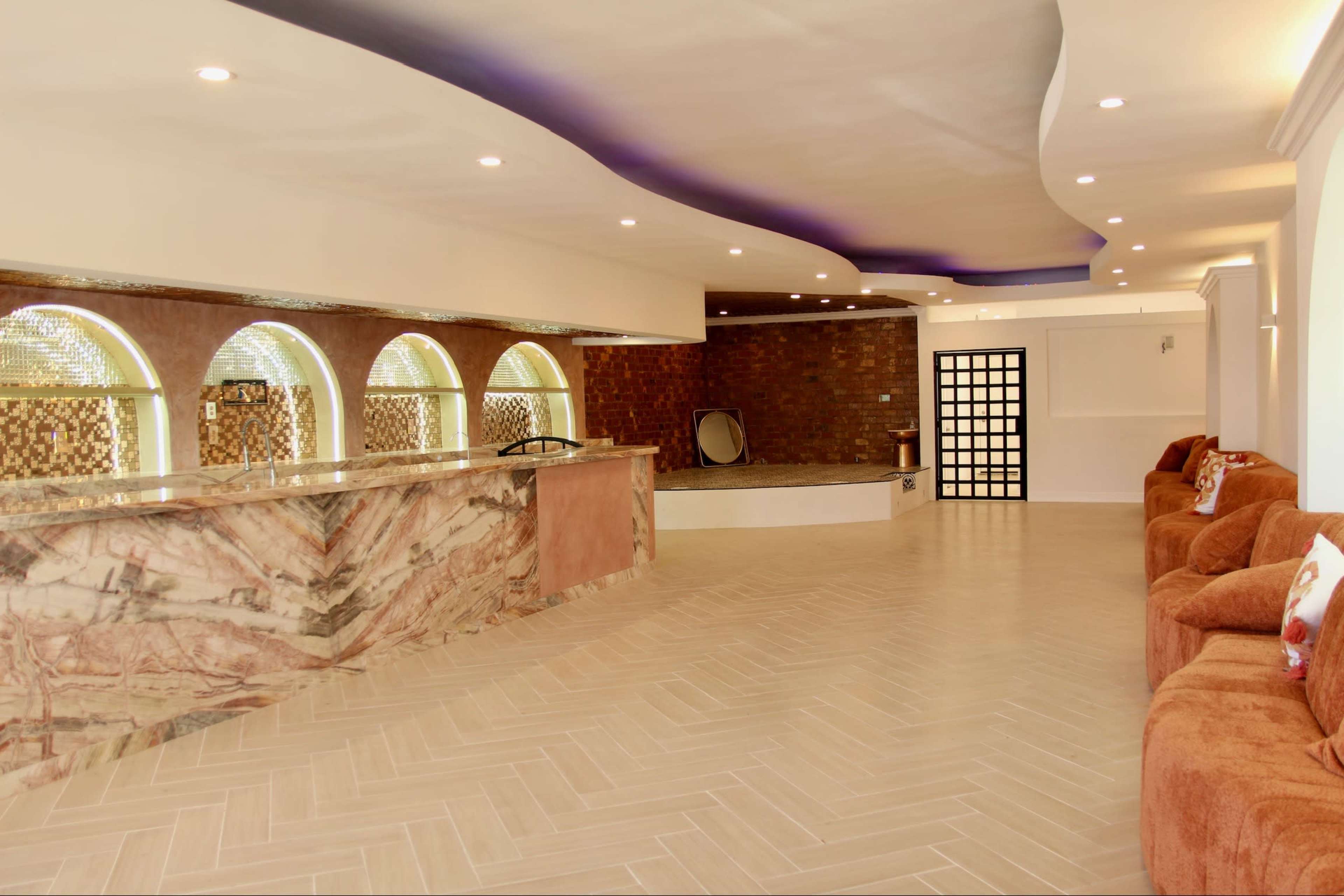 The image shows a spacious interior featuring a reception area with a marble counter, arched windows, and a seating arrangement along the wall.