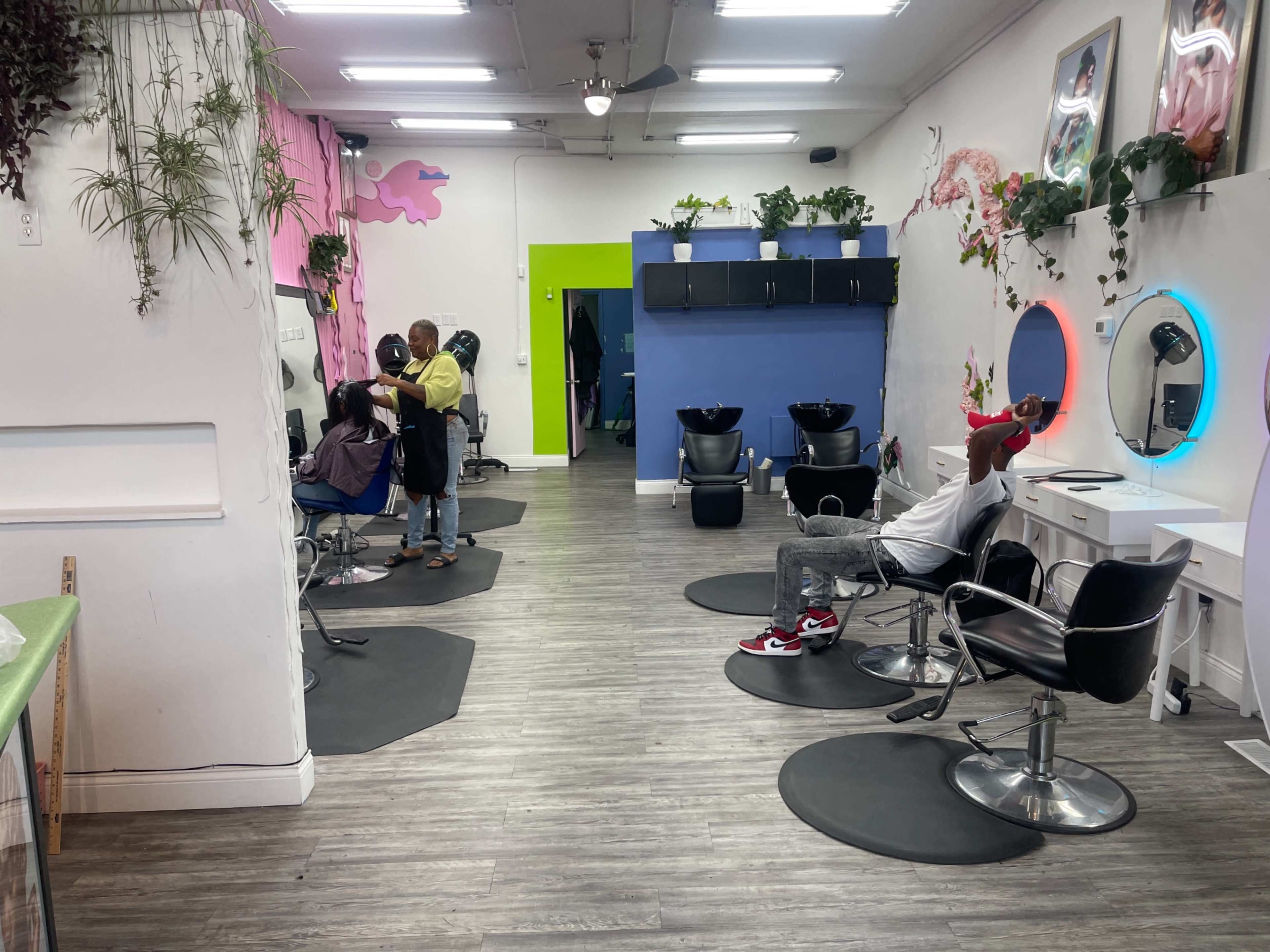 The interior of a hair salon features several stylist chairs with clients, mirrors, and vibrant wall decorations in various colors.