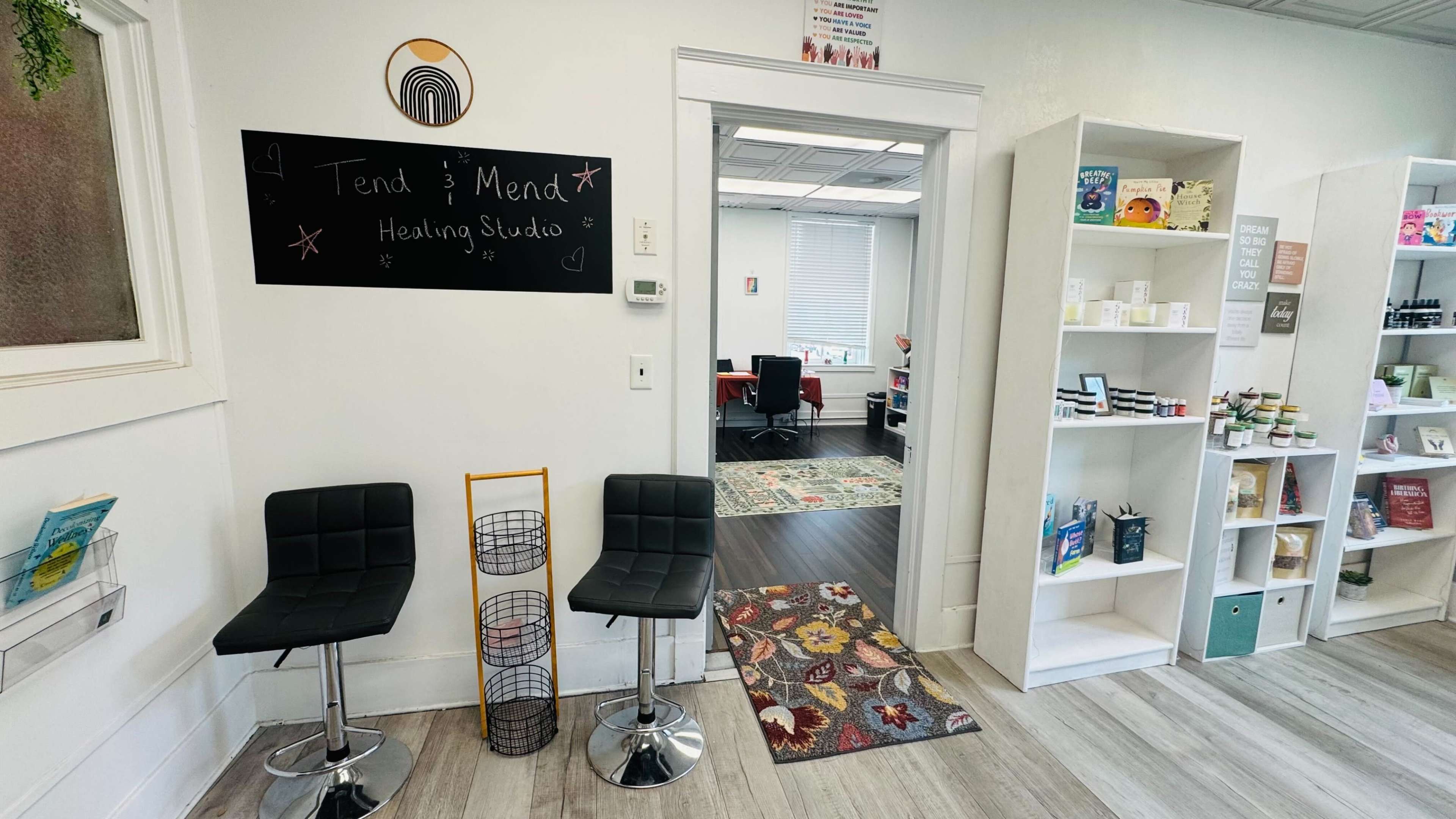 The image shows a small wellness studio entrance with black stools, a chalkboard sign that reads "Tend & Mend Healing Studio," and shelves displaying various products.