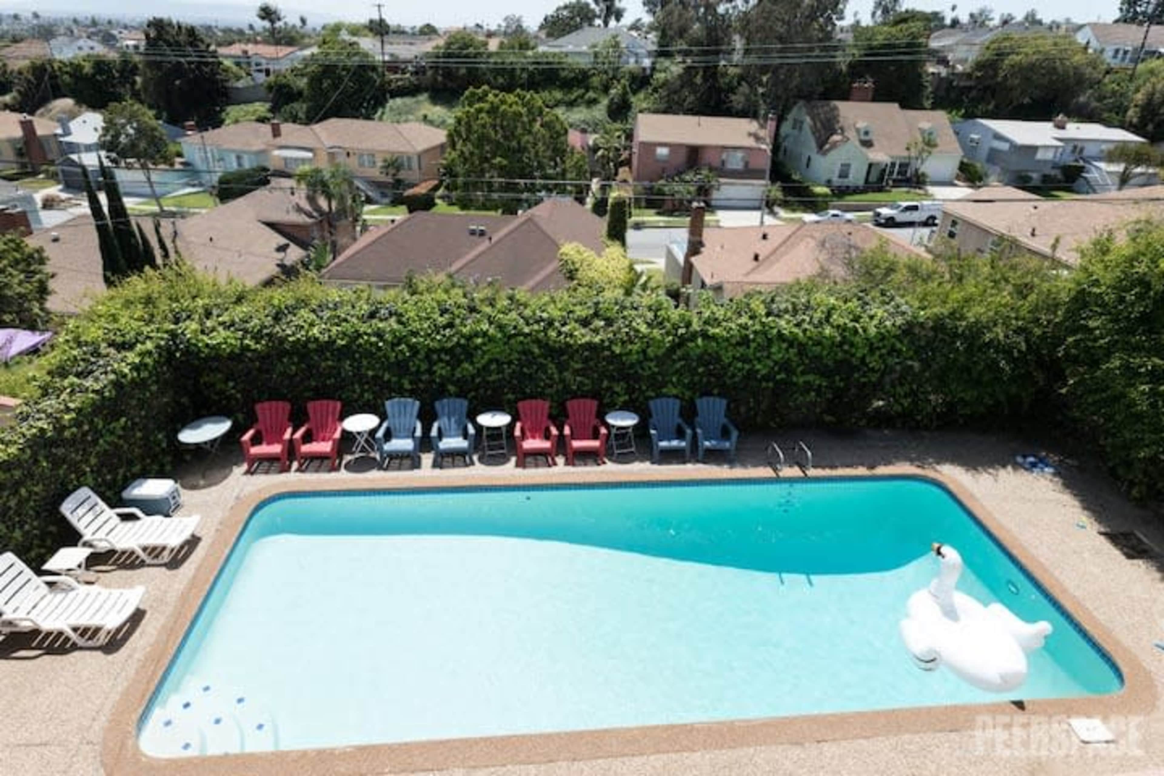 An aerial view of a backyard swimming pool surrounded by lounge chairs and a large white inflatable swan.
