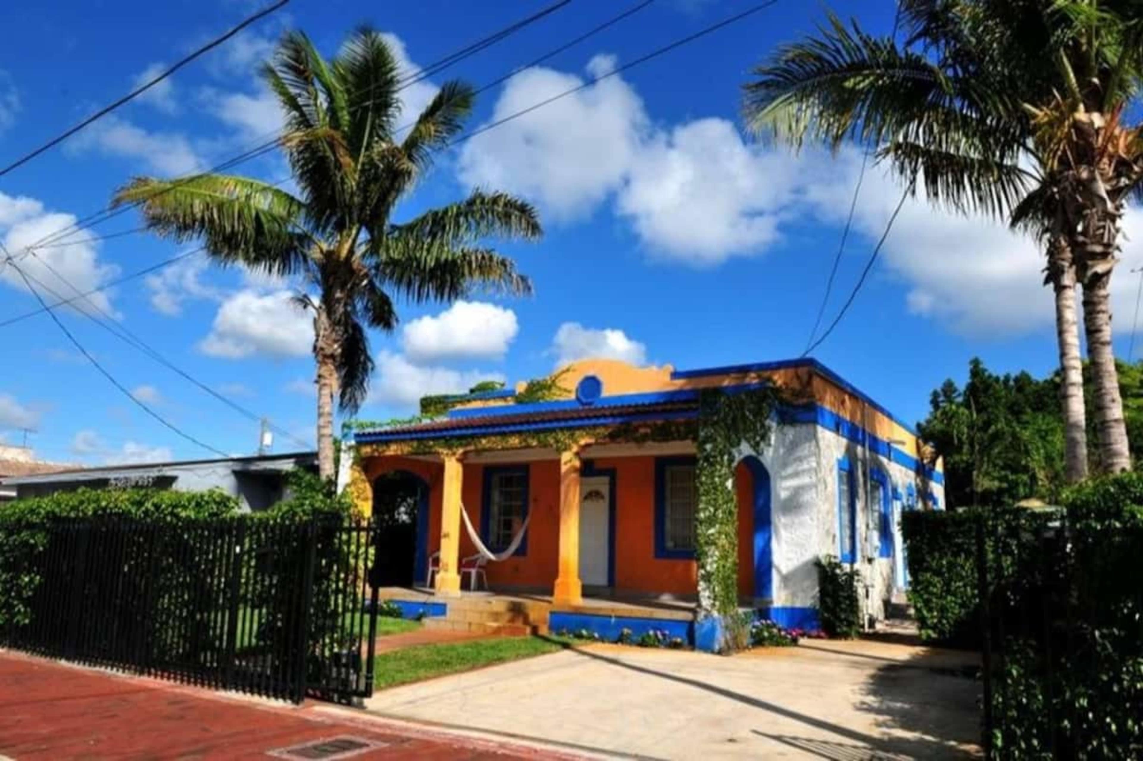 A colorful house with blue and orange accents is surrounded by palm trees and clear blue skies.