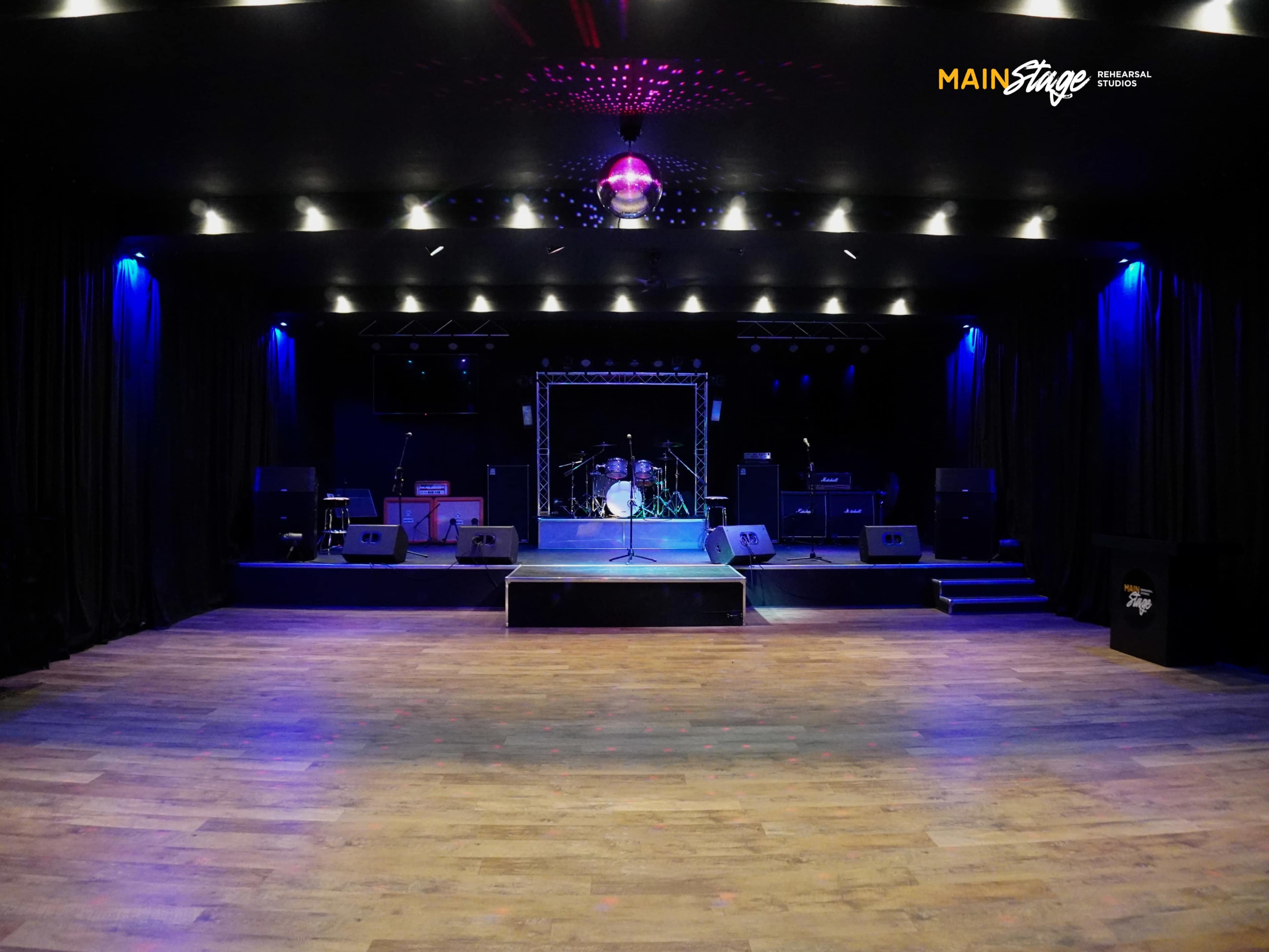 A stage is set with musical instruments and amplifiers, illuminated by blue lights in a dark venue.