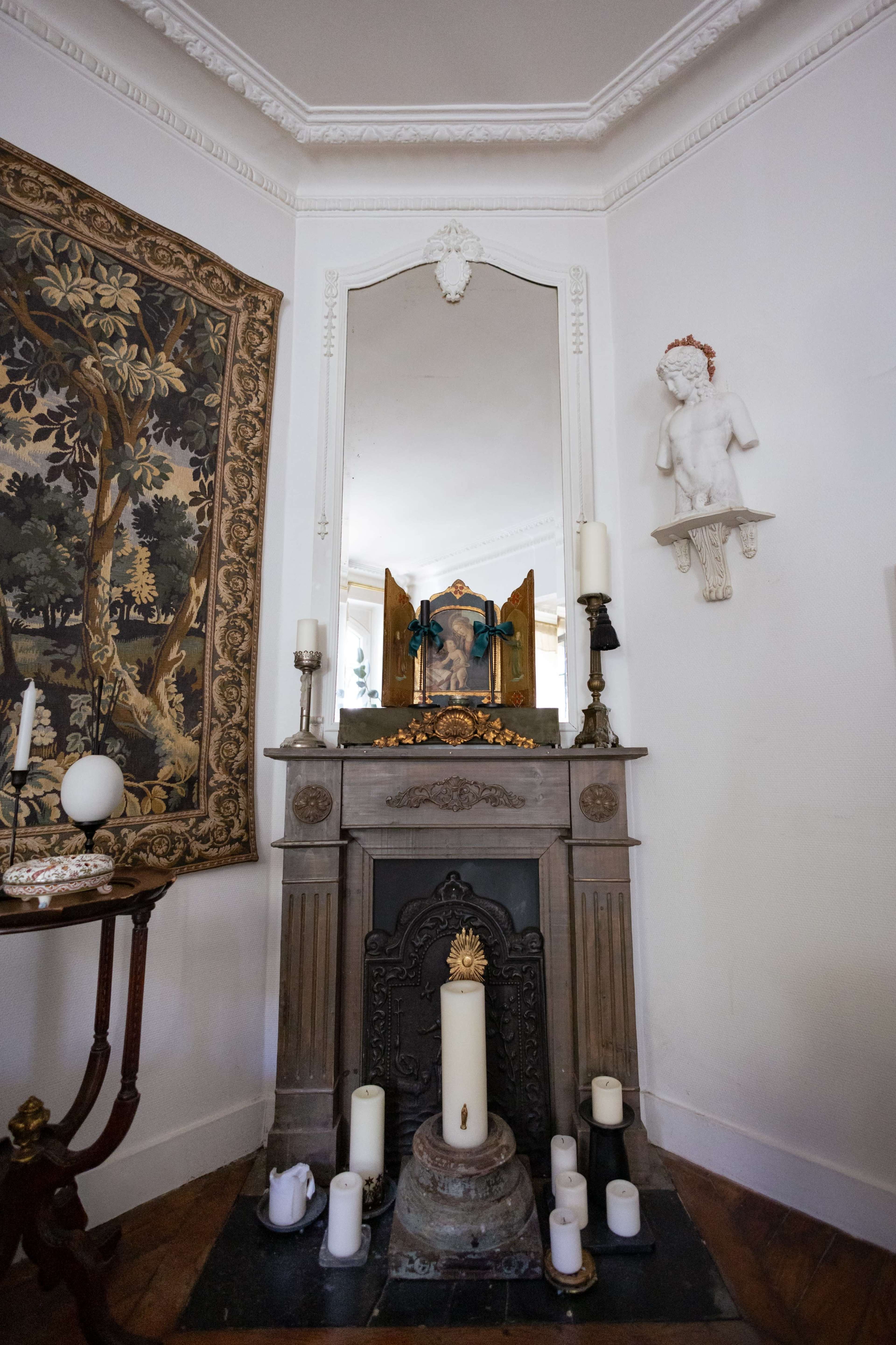 The image shows an ornate fireplace with a large mirror above it, surrounded by decorative candles, a wall tapestry, and a statue.