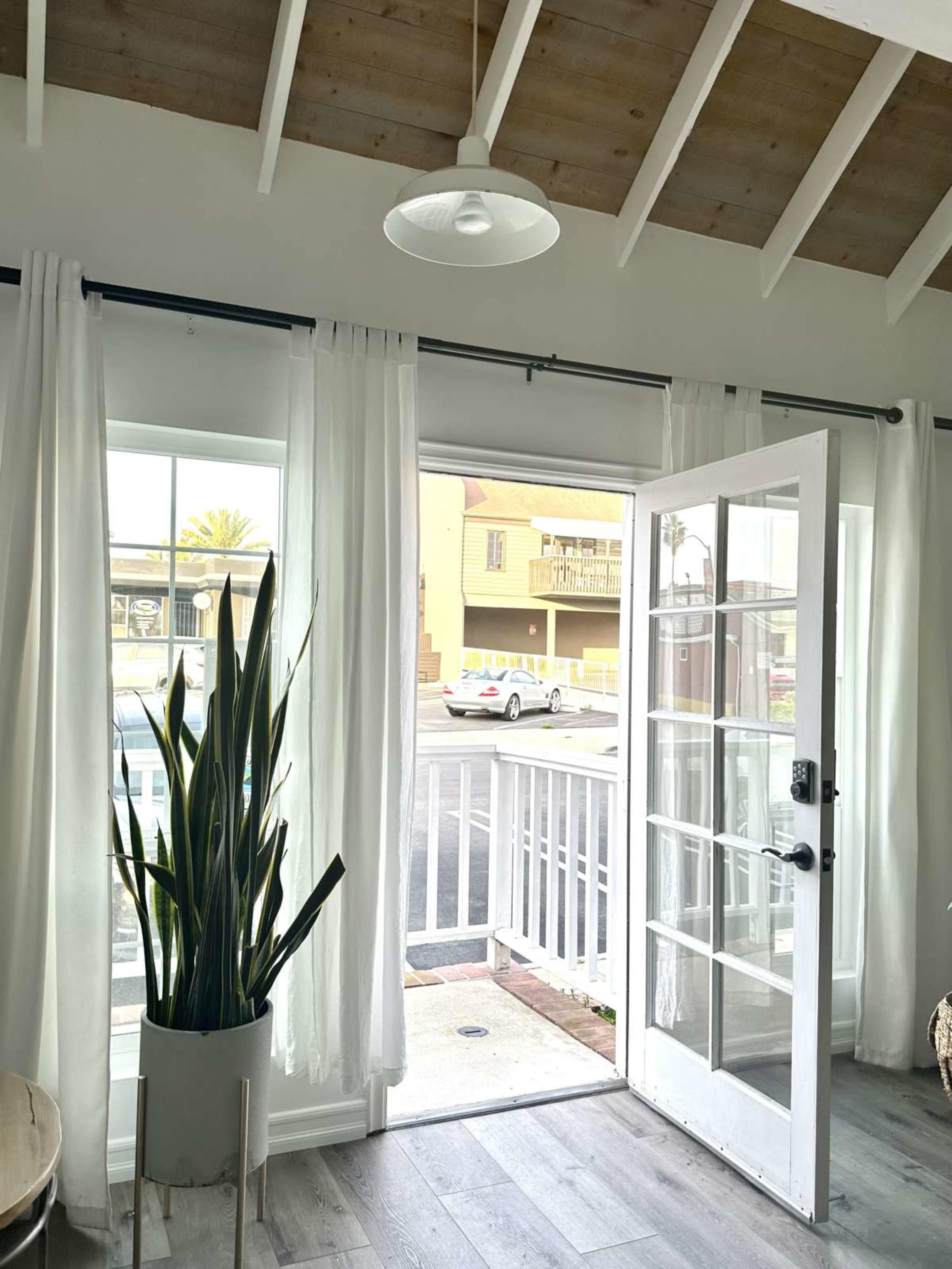 A bright interior room features sheer white curtains, a potted plant, and a partially open door leading to an outdoor area.
