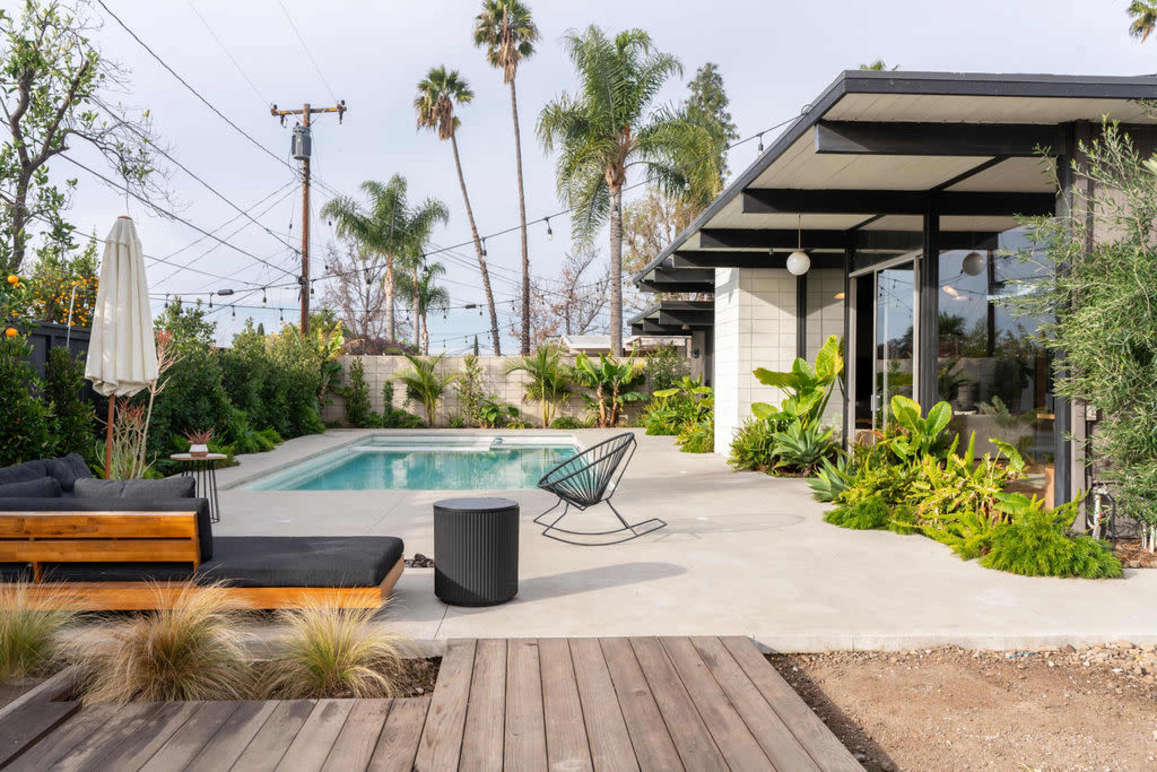 The image displays a modern home with a swimming pool surrounded by lush greenery and outdoor seating.