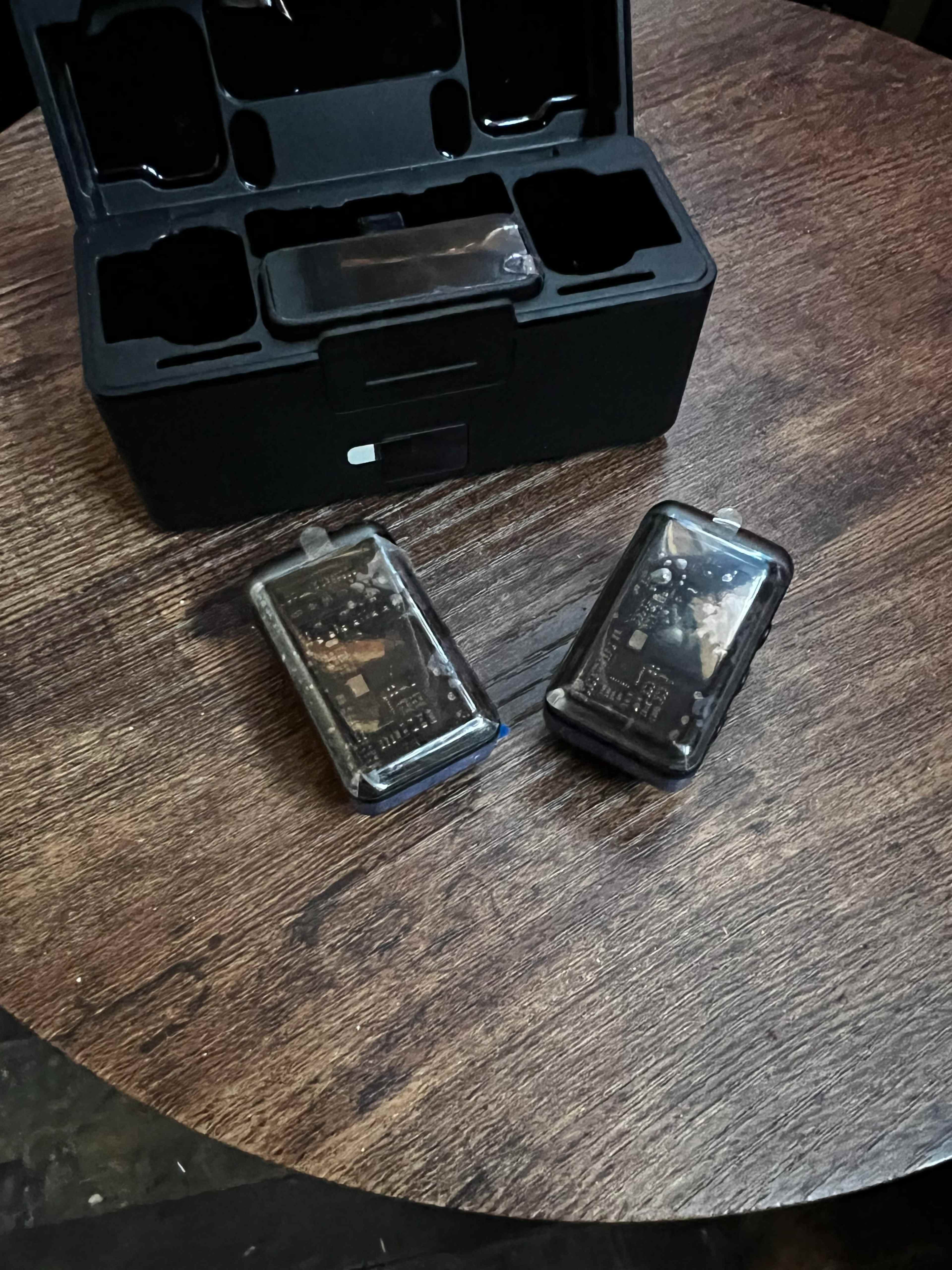 The image shows a black storage case with two transparent electronic device cases resting on a wooden surface.