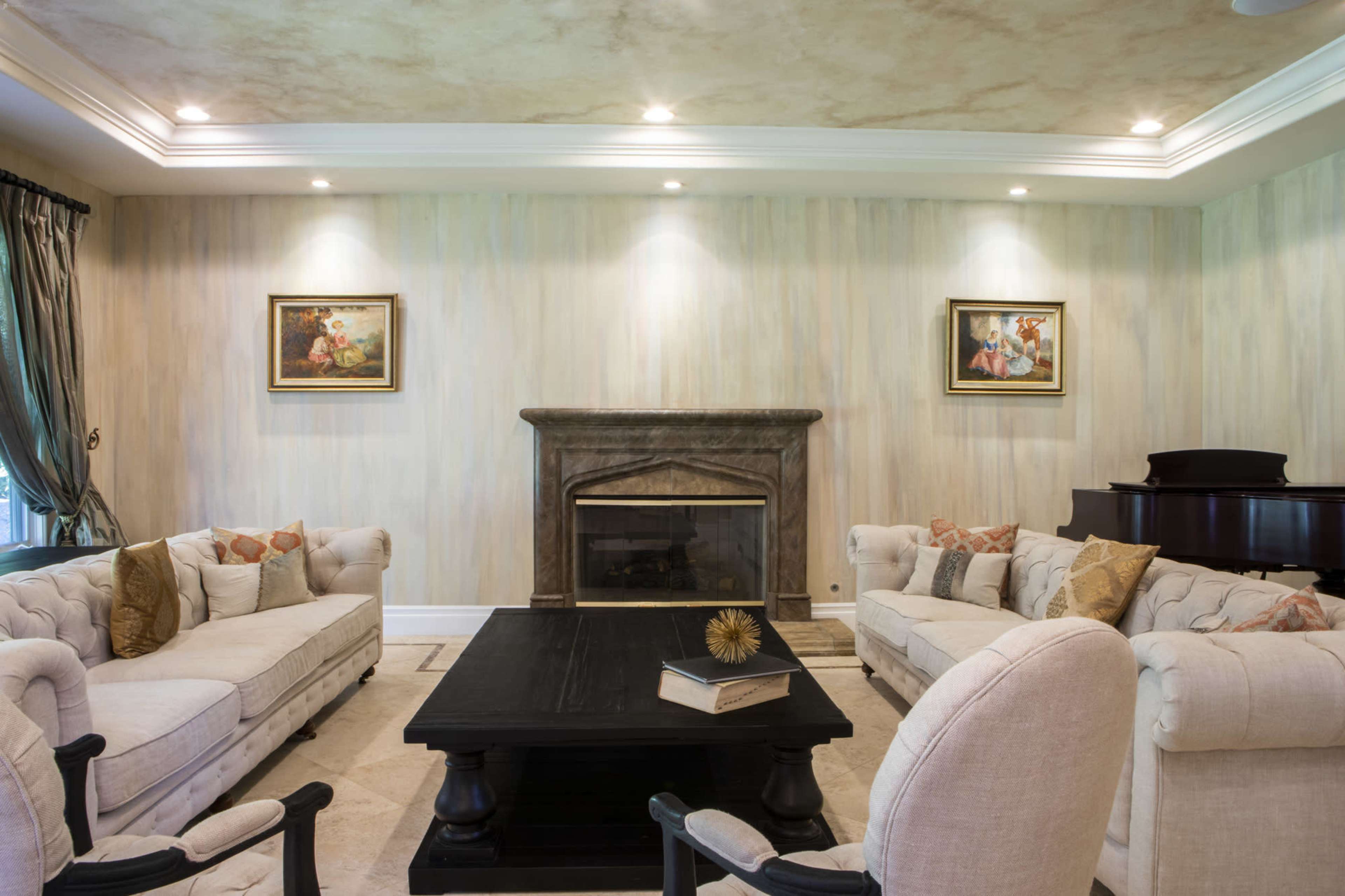 A living room with two upholstered sofas facing a black coffee table, a fireplace with a stone mantel, and framed paintings on the walls.