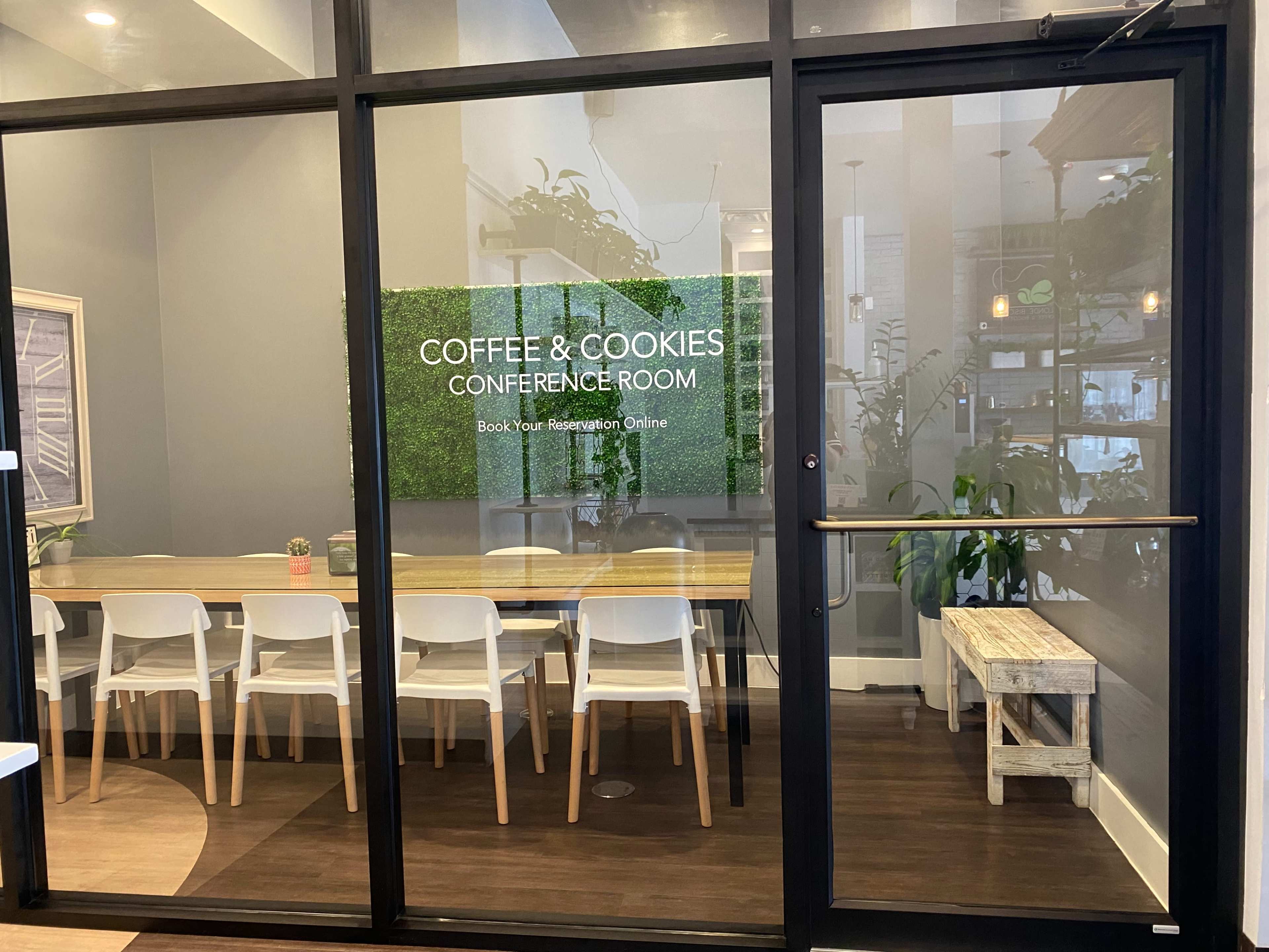 A conference room with a large table surrounded by white chairs, enclosed by glass walls and a sign that reads "Coffee & Cookies Conference Room."