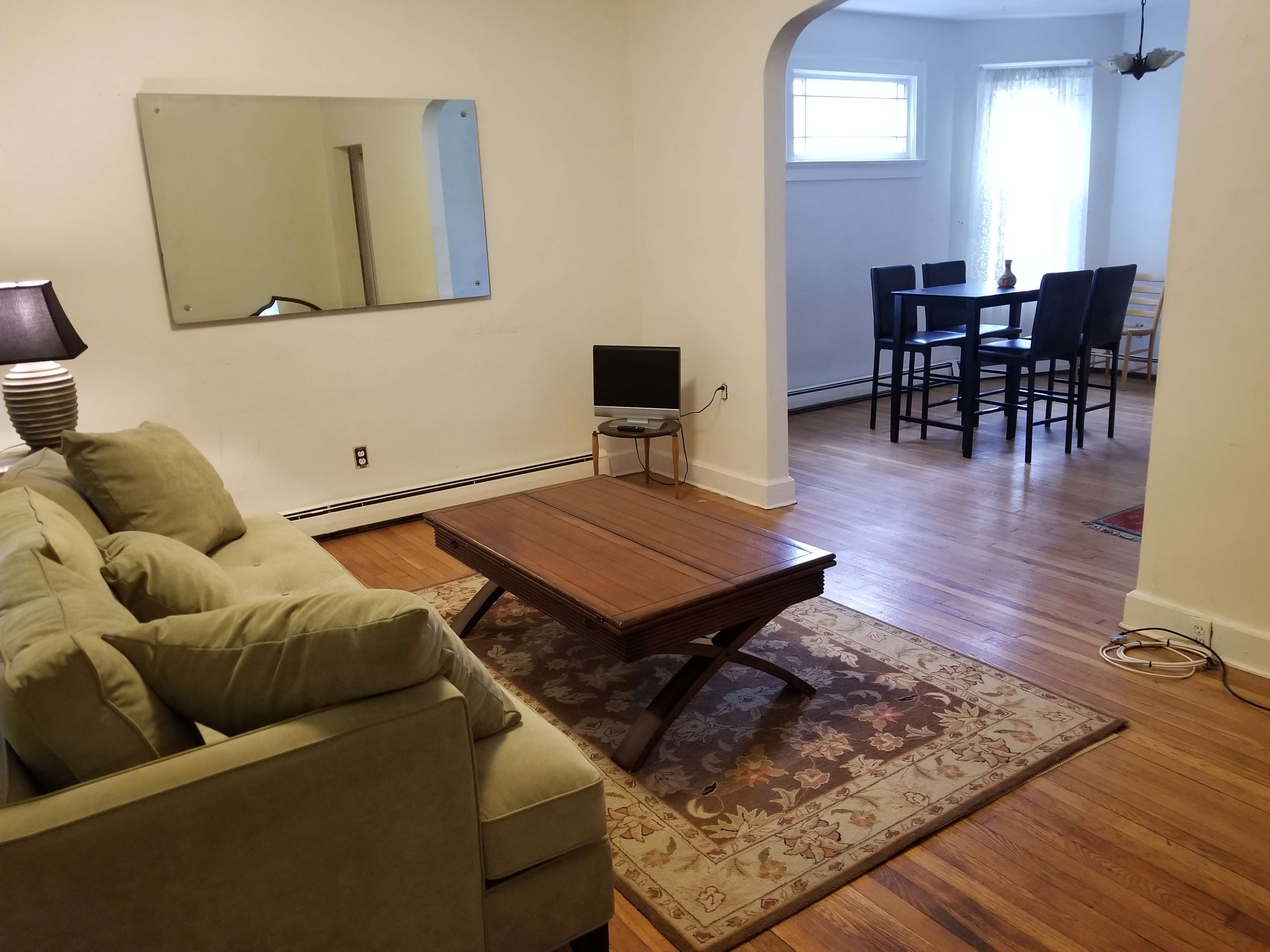 A living room area with a green sofa and a wooden coffee table, leading into a dining space with a small table and chairs.