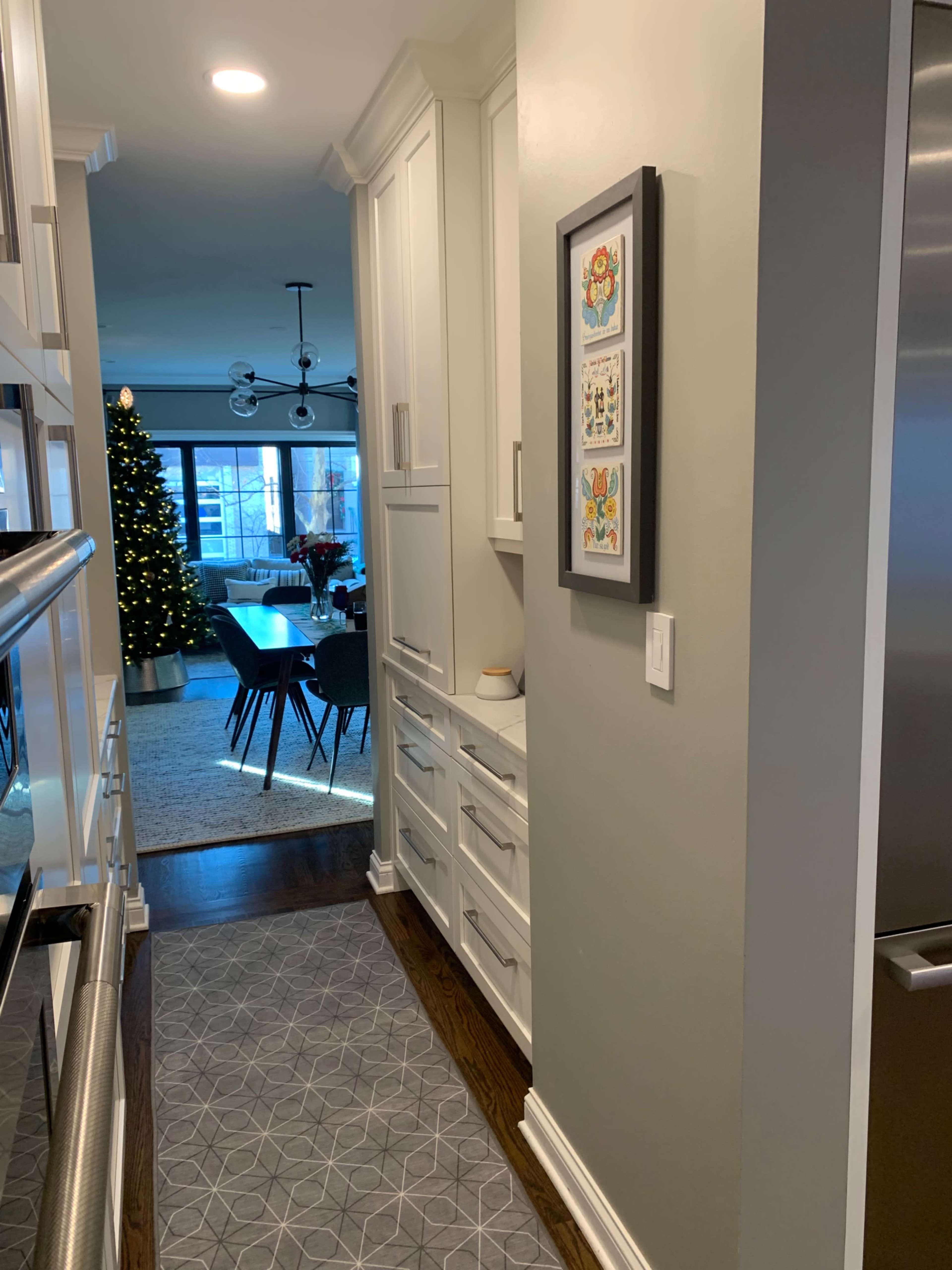 The image shows a narrow hallway leading to a living area with a dining table and a Christmas tree in the background.