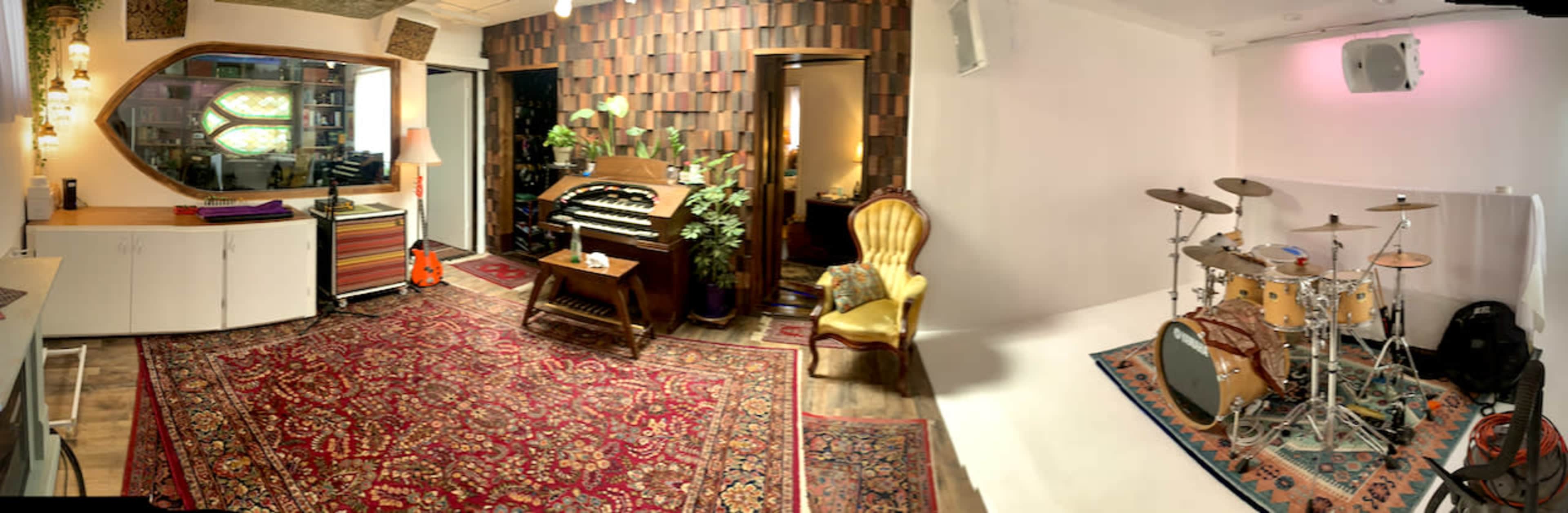 A spacious studio room featuring a vintage organ, a drum set, a yellow armchair, and decorative rugs.