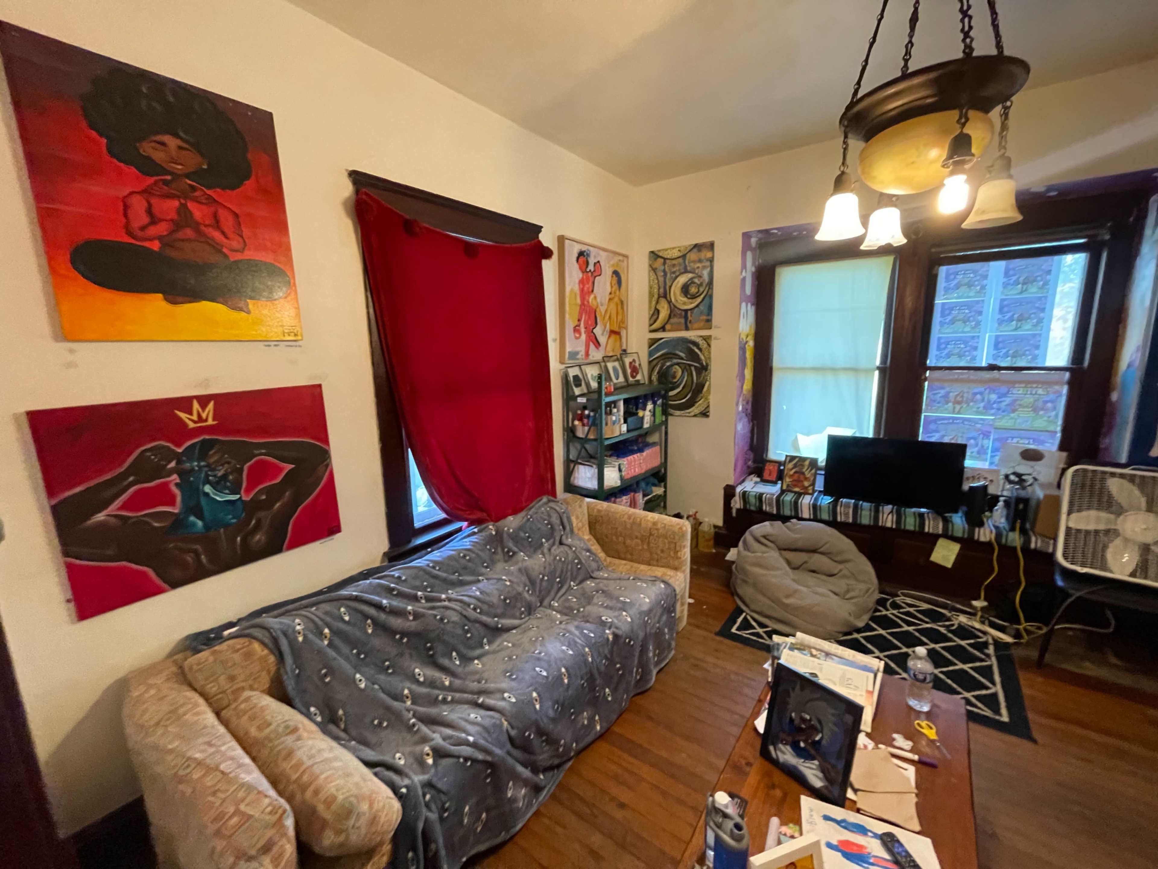 The living room features a patterned sofa, colorful artwork on the walls, and a coffee table in front of a window.