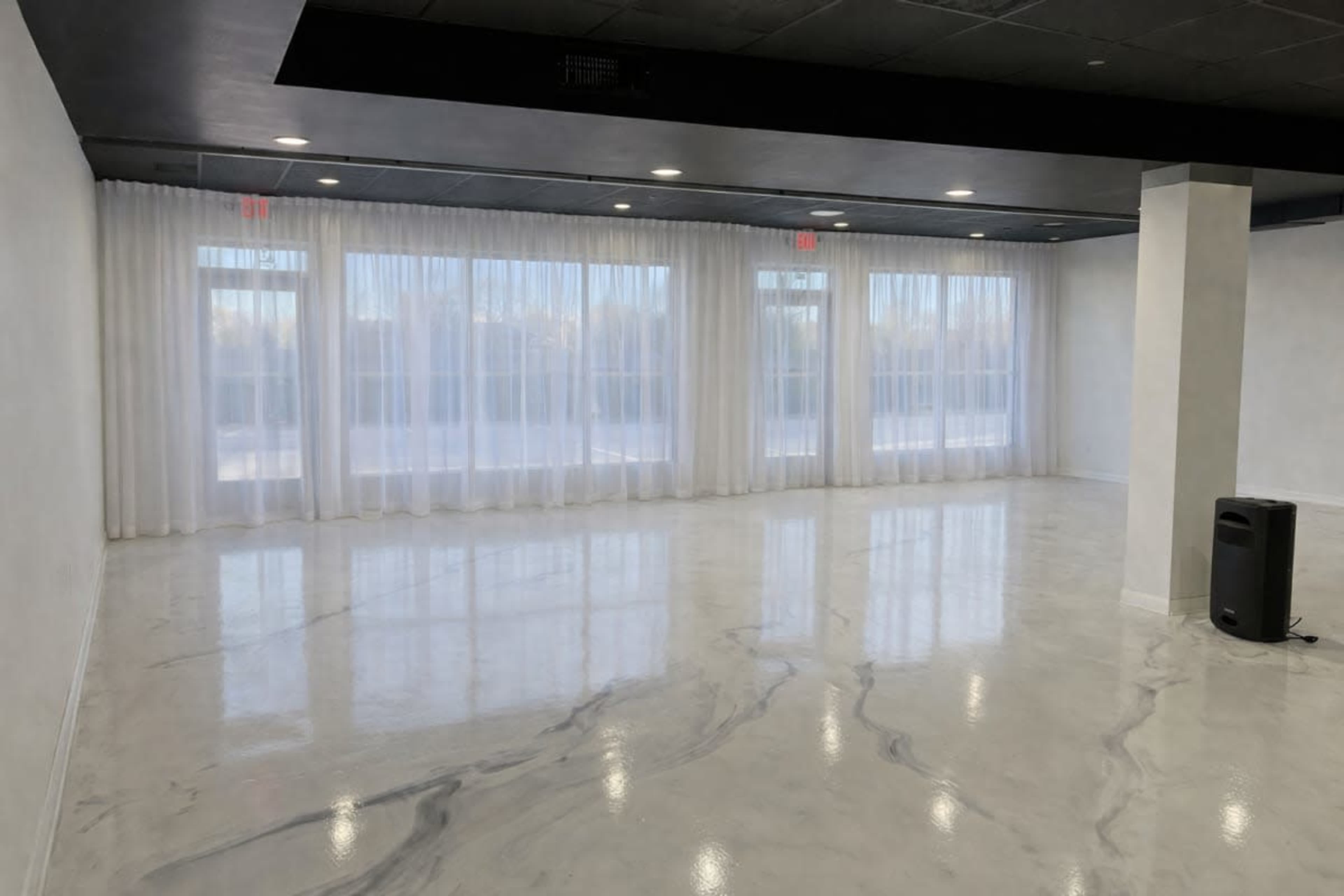 The image shows an empty room with polished marble flooring and large windows covered by sheer white curtains.