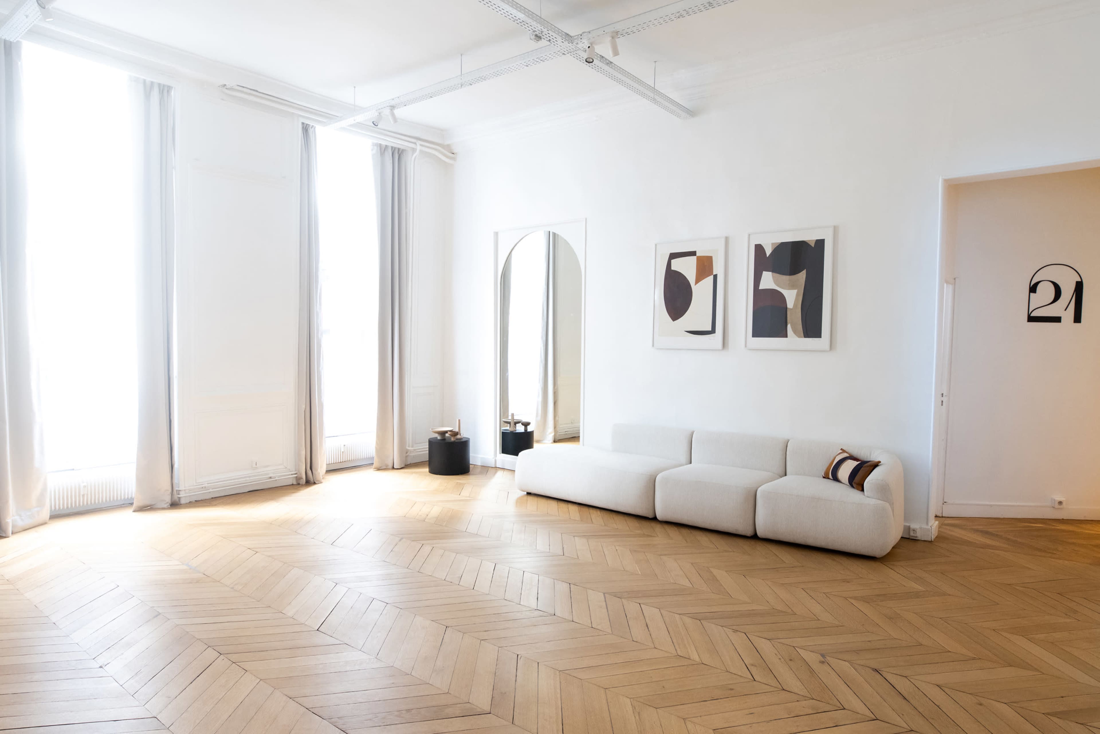 A spacious room with large windows, light-colored walls, a curved fabric sofa, and two framed artworks on the wall.