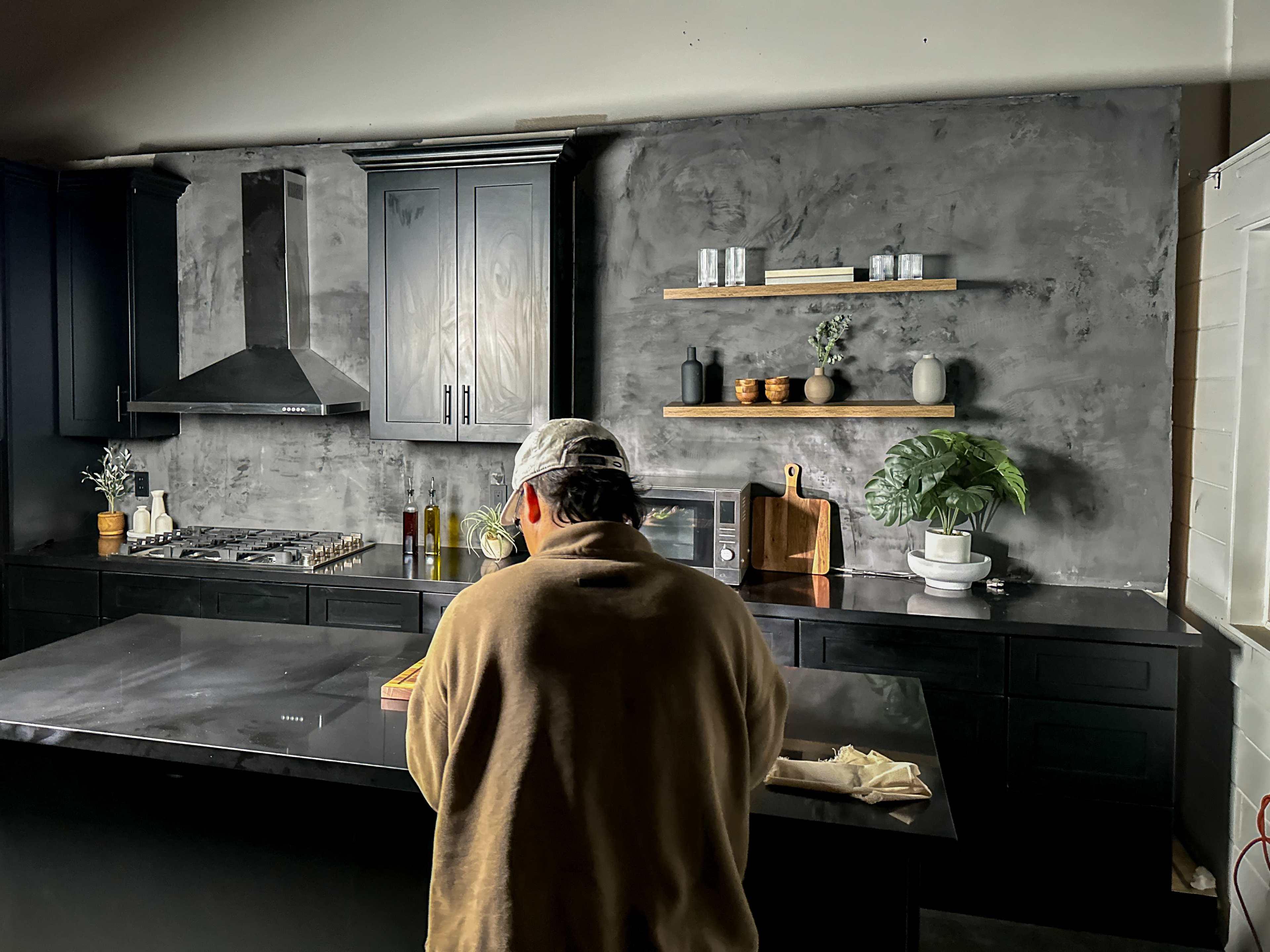 A person stands at a kitchen island, preparing food in a modern kitchen with dark cabinets and minimalistic decor.