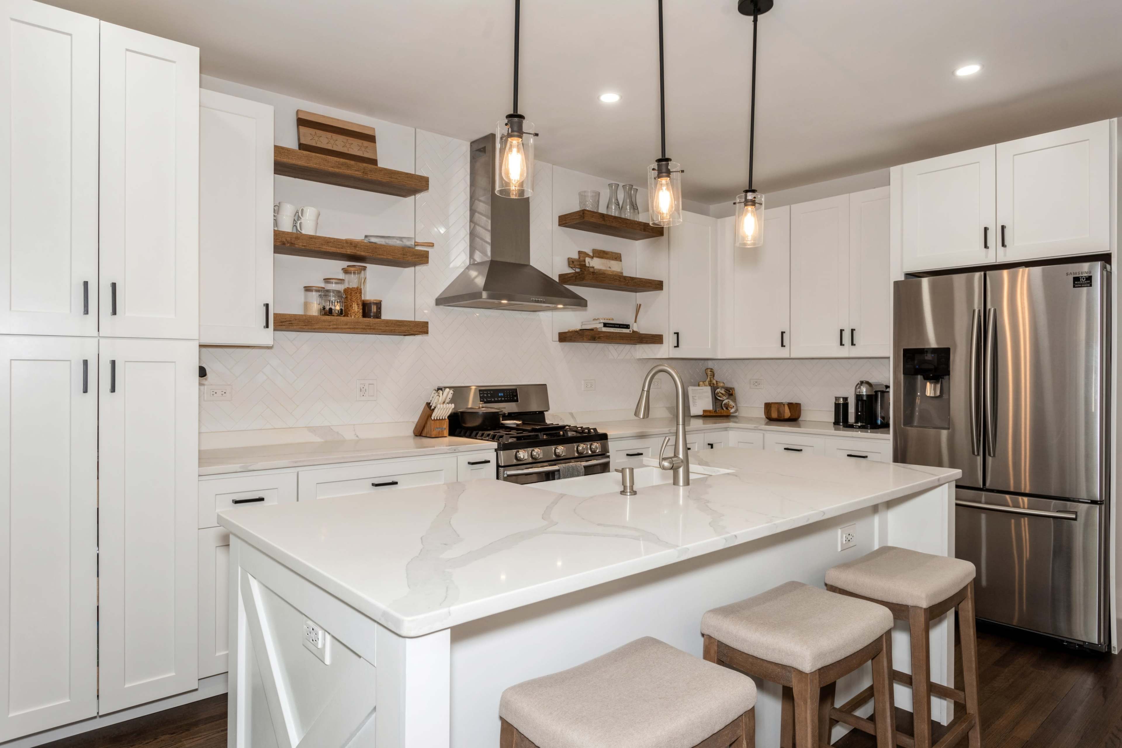 A modern kitchen featuring white cabinetry, a large island with seating, and open shelves displaying kitchenware.