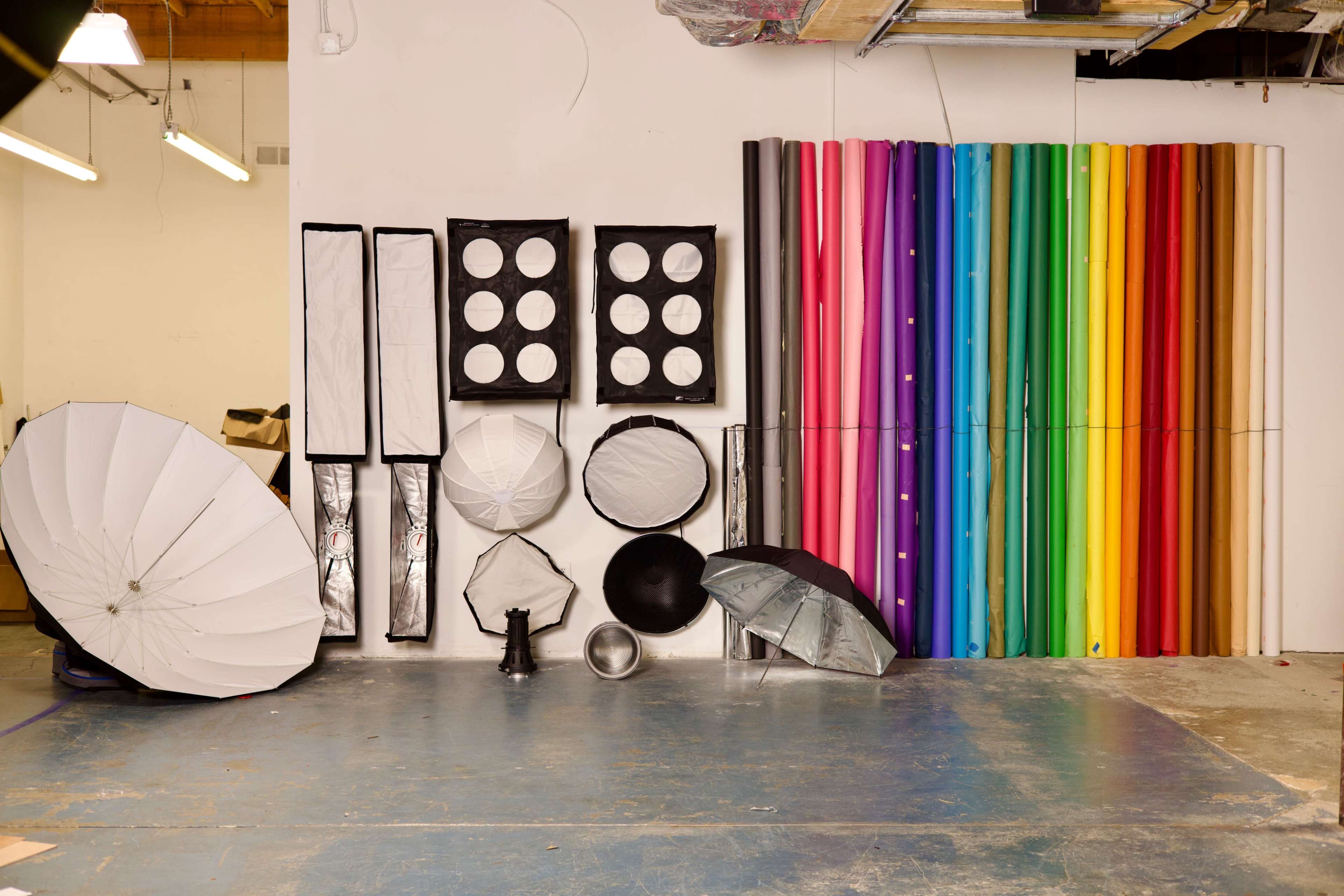 A variety of photography equipment arranged on a wall, including light modifiers, backdrops, and umbrellas.