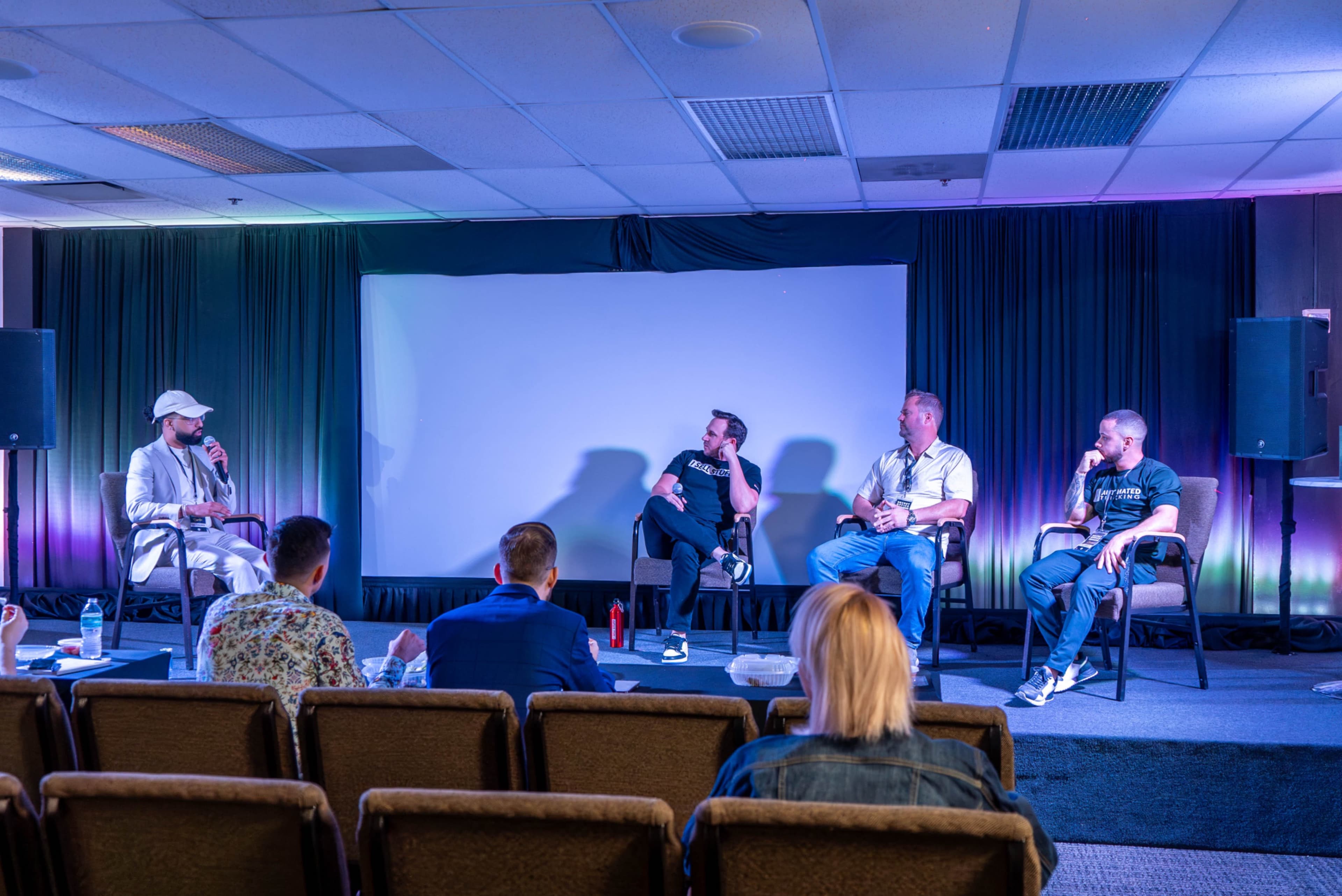 A panel discussion features four speakers addressing an audience seated in rows.