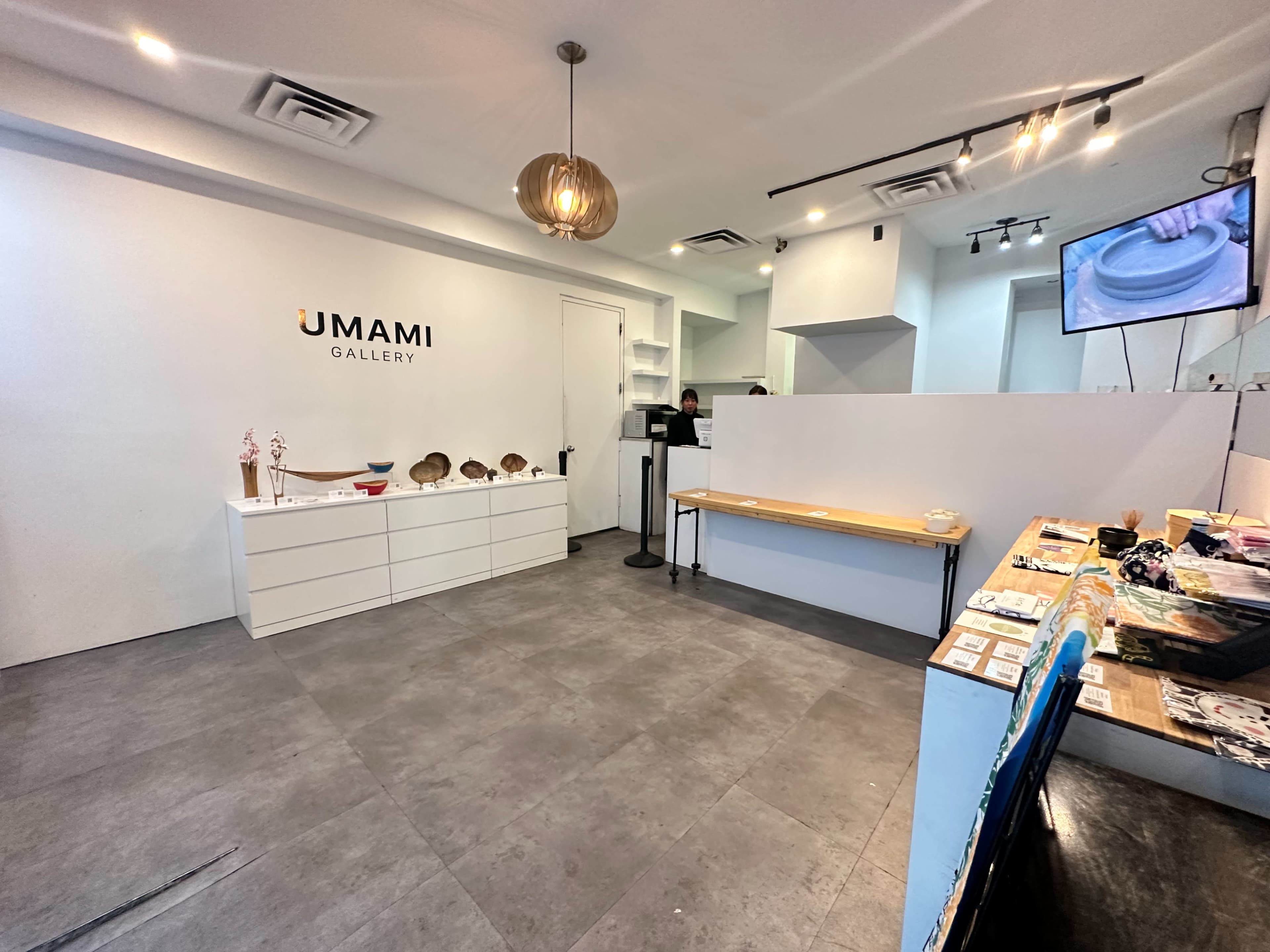 A modern gallery space featuring a reception area, display shelves, and various art items on a table.
