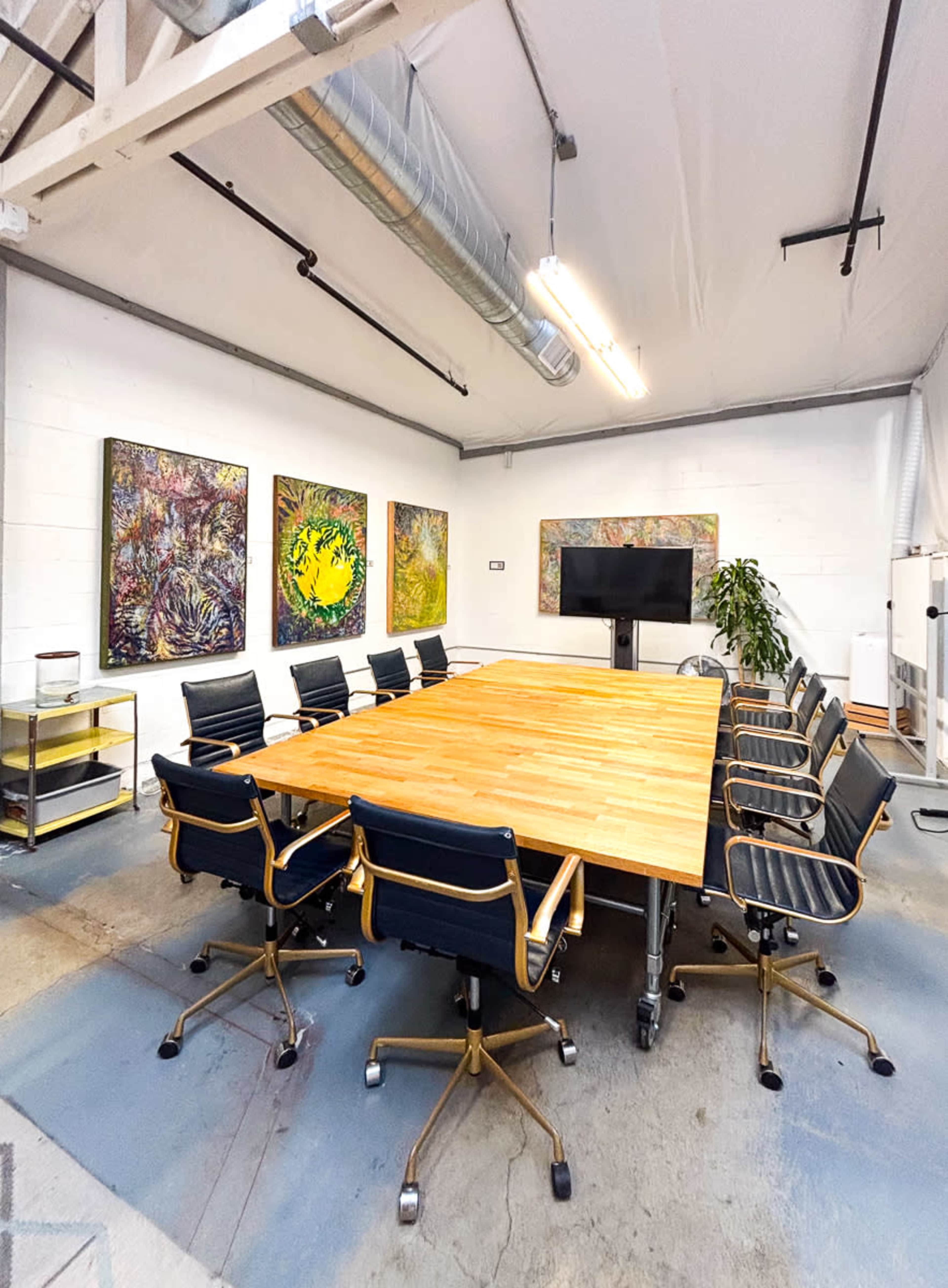 The image shows a spacious conference room with a large wooden table surrounded by black office chairs and colorful abstract artwork on the walls.